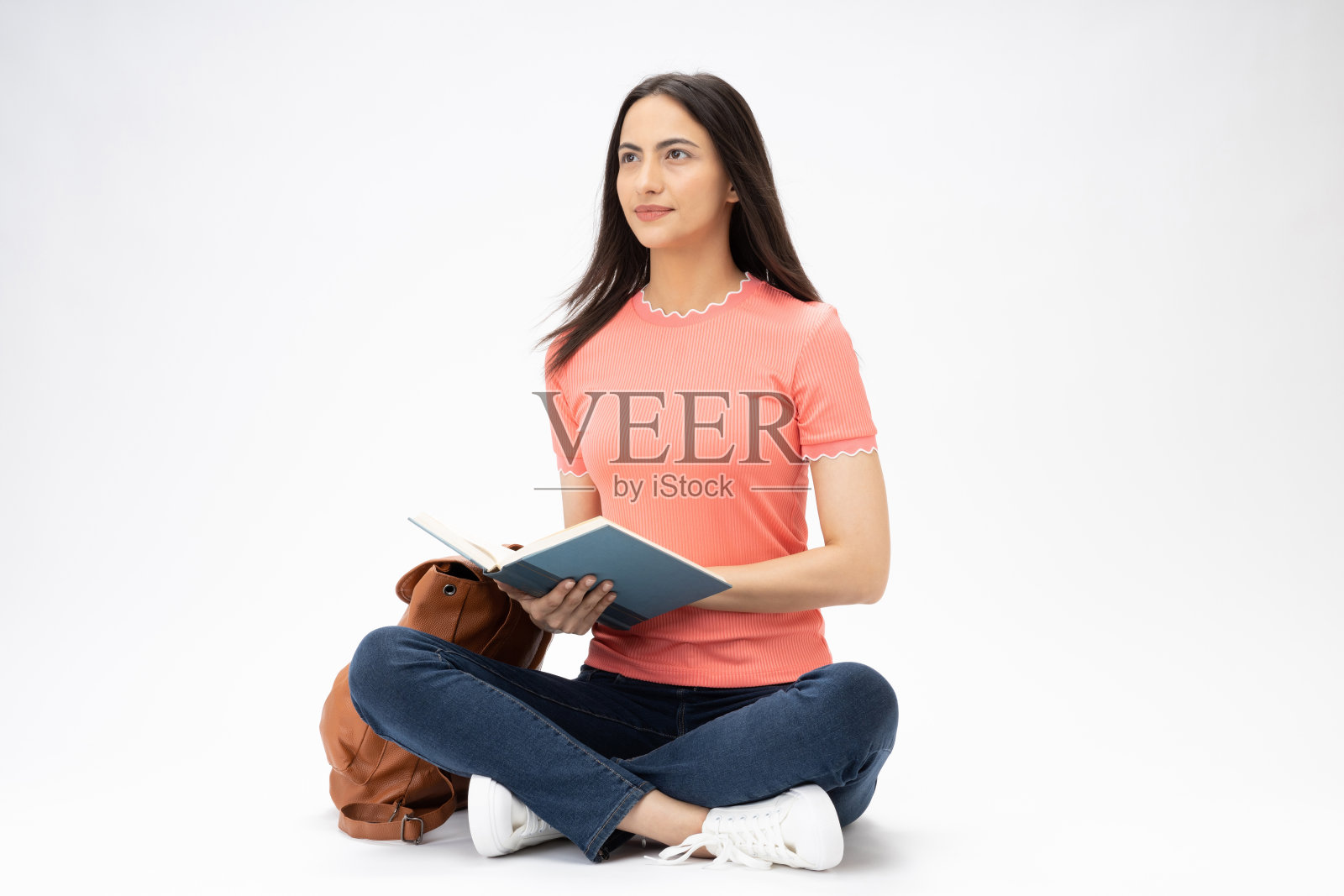 全身尺寸的年轻女孩读书坐在地板上穿着牛仔裤牛仔粉t恤鞋孤立在白色背景股票照片照片摄影图片