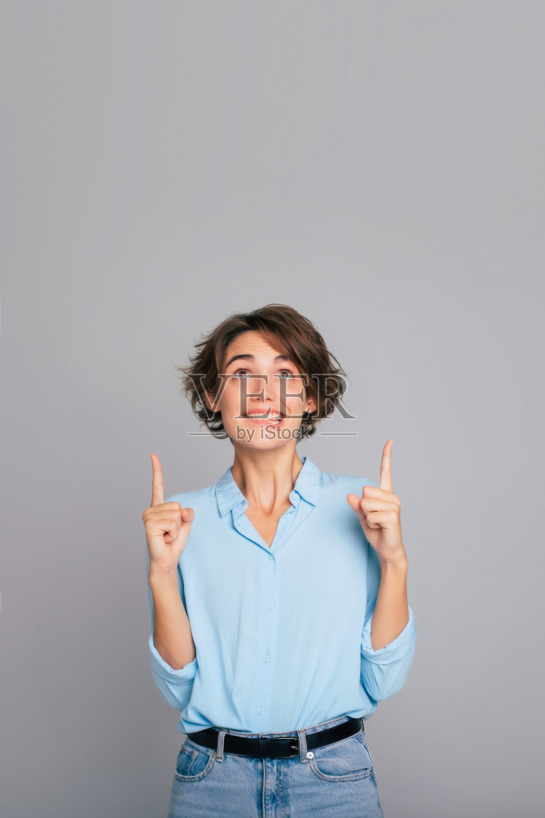 照片正面的黑发女子点以上显示的地方为您的广告文字微笑愉快穿着智能休闲隔离在灰色背景照片摄影图片