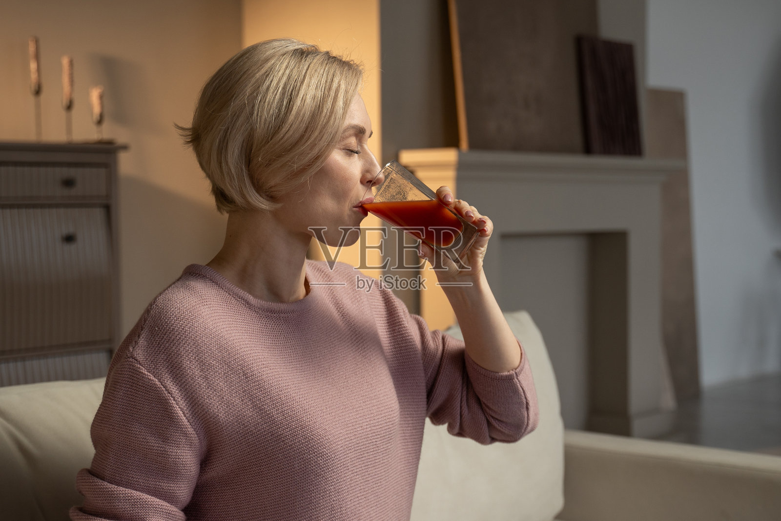 黄昏时分，一个女人在舒适的客厅里品尝着一杯番茄汁照片摄影图片