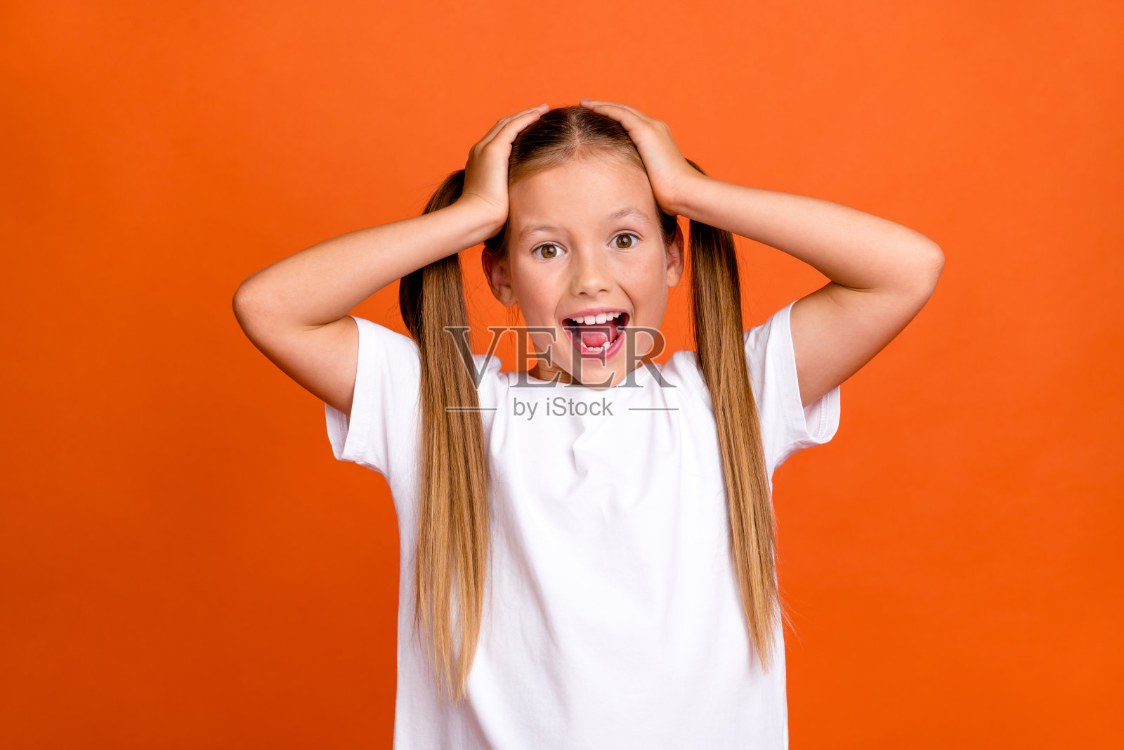 照片中可爱的小女孩摸着头震惊地喊着穿着时髦的白色衣服孤立在橙色的背景照片摄影图片