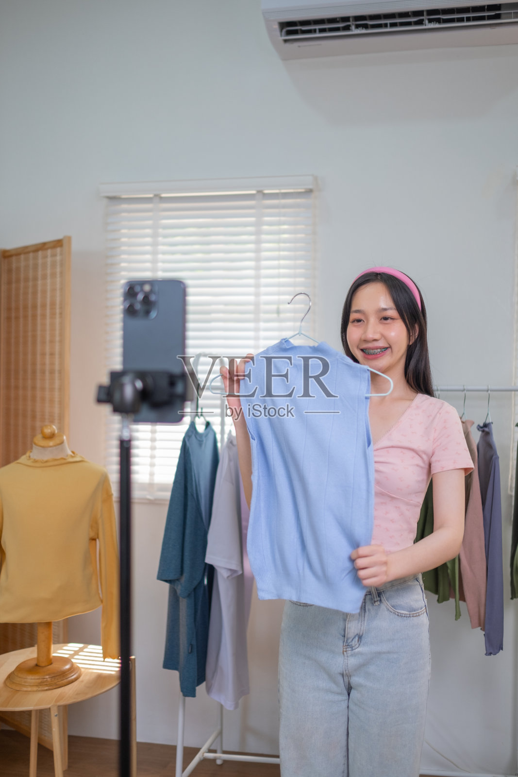 年轻的亚洲女性在线卖家正在使用智能手机在网上直播，介绍新的时尚布衬衫新系列，并与客户交谈照片摄影图片