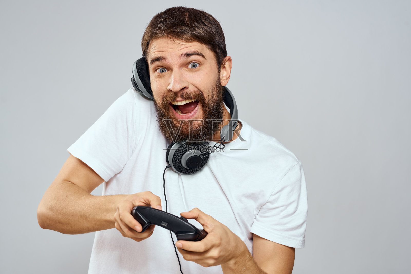 男子带着游戏手柄耳机玩休闲科技白t恤浅色背景照片摄影图片