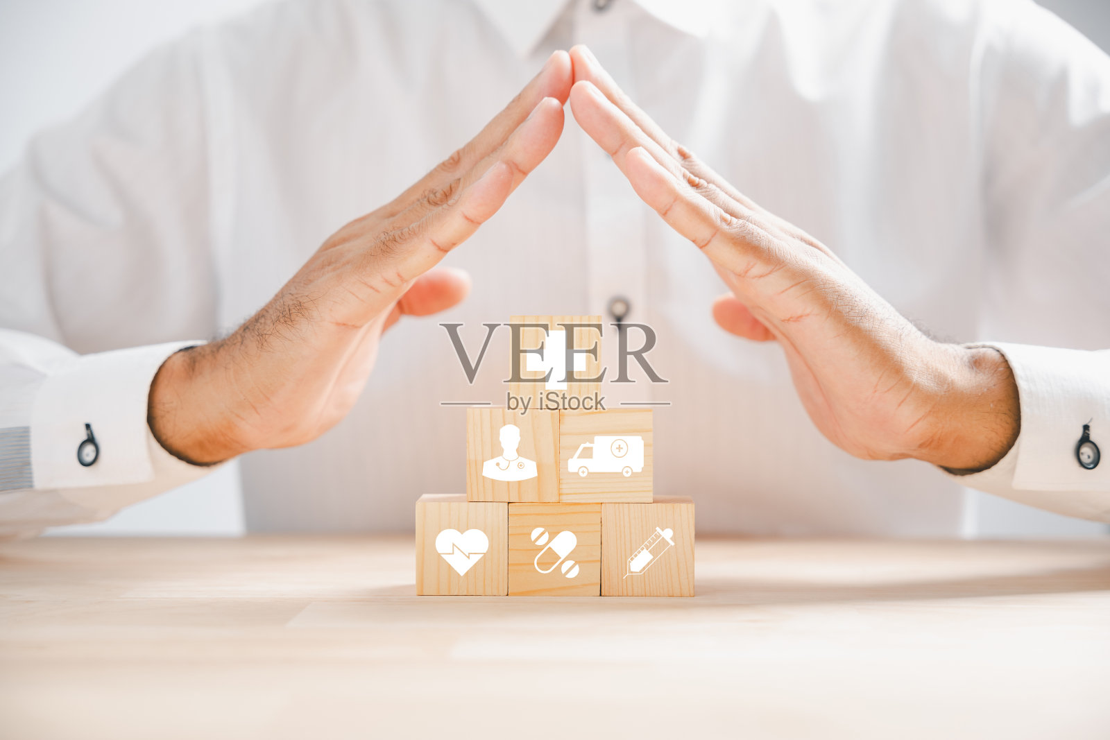 医疗保健和保险的象征性代表，通过一个医生的手在一个带有保护标志的木制立方体块。堆叠的医疗图标展示全面的医疗服务。医疗保健理念照片摄影图片