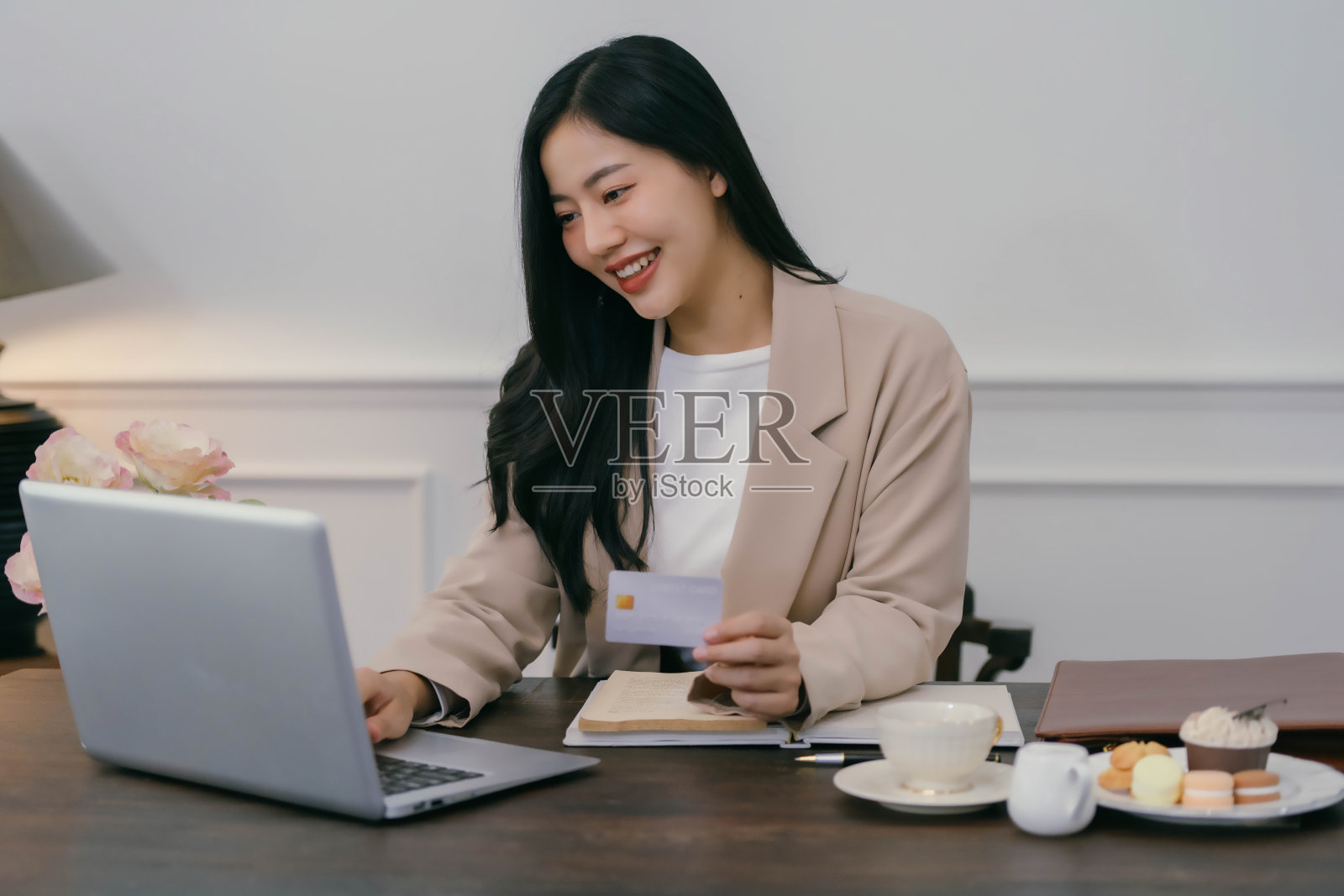 一个女人坐在桌子前，手里拿着笔记本电脑和信用卡照片摄影图片