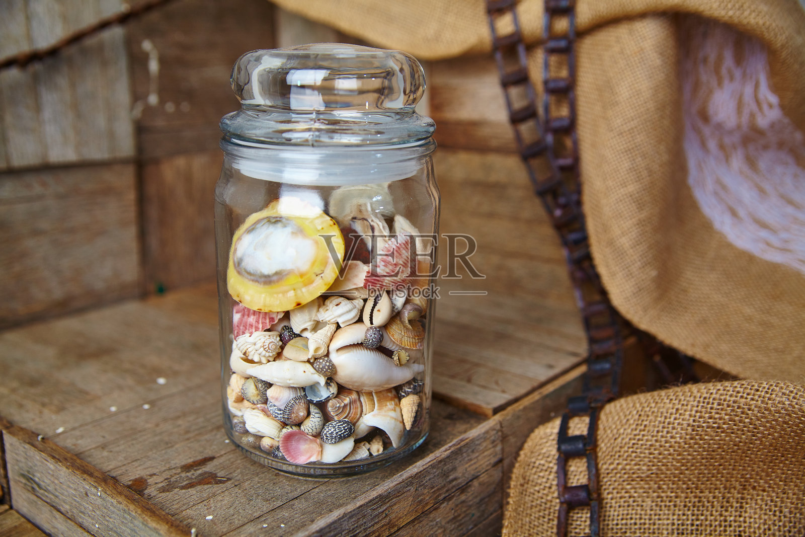 以粗麻布为背景的质朴木材上的玻璃罐贝壳收藏照片摄影图片