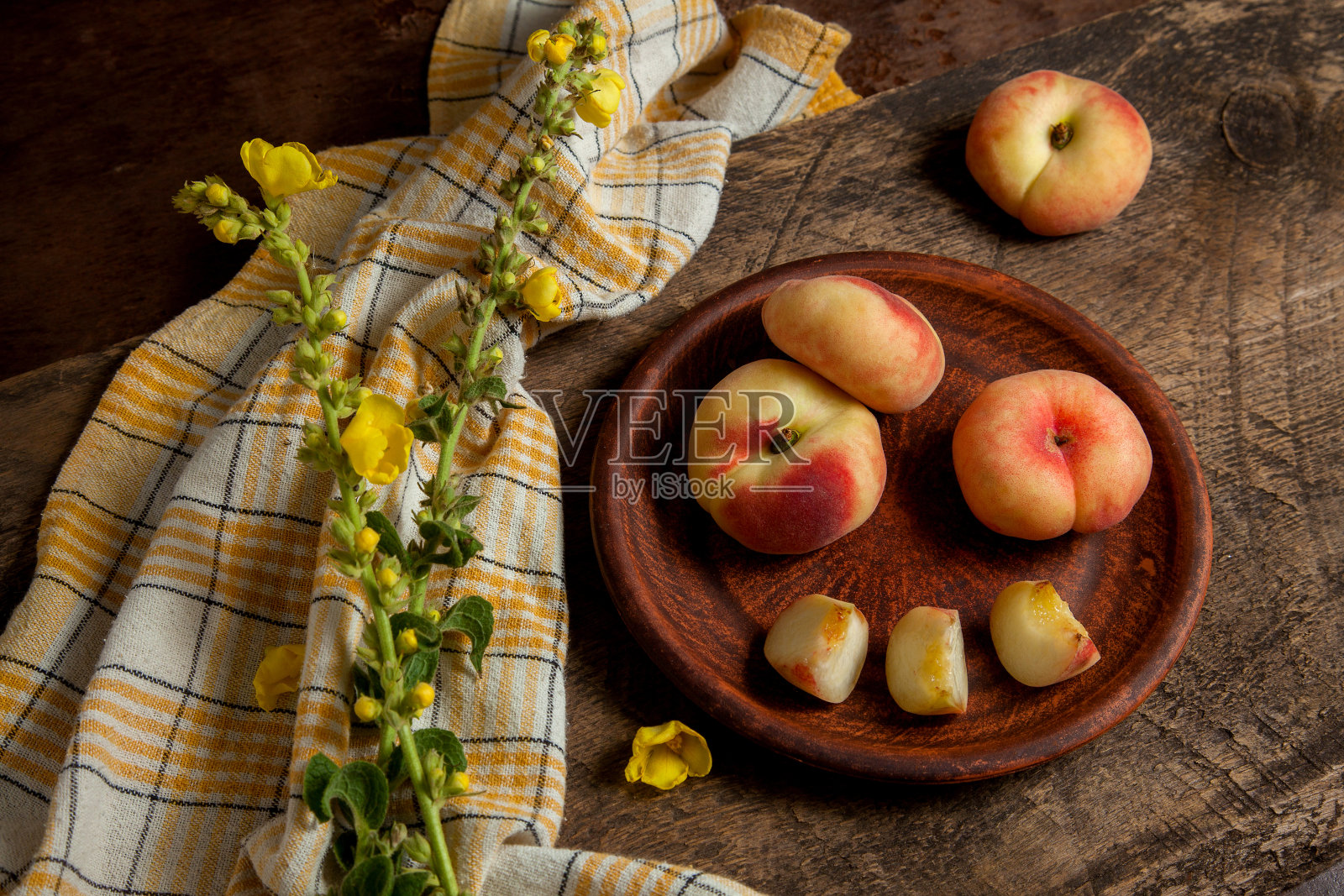 粘土板与切割和整个土星桃子或扁桃子木制背景与黄色厨房毛巾。照片摄影图片