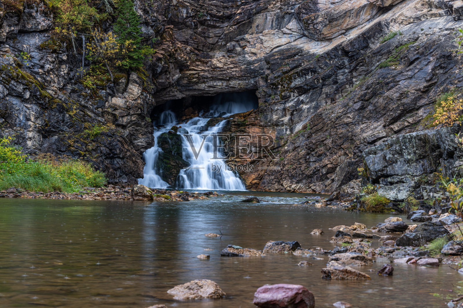 瀑布流入河流，河岸是岩石照片摄影图片