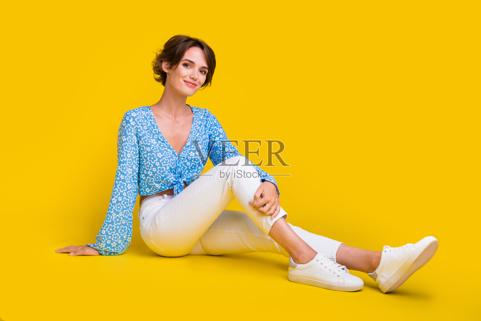 可爱的漂亮乐观的女人穿蓝色上衣白色裤子坐在地板上孤立的黄色背景的全尺寸照片照片摄影图片