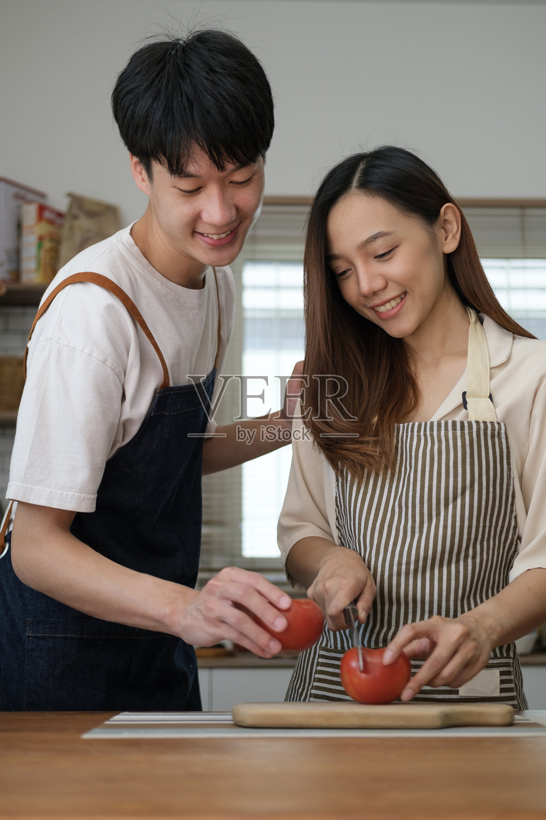 快乐的年轻夫妇穿着休闲的衣服在现代厨房一起准备晚餐，生活方式，休闲和爱情的概念。照片摄影图片