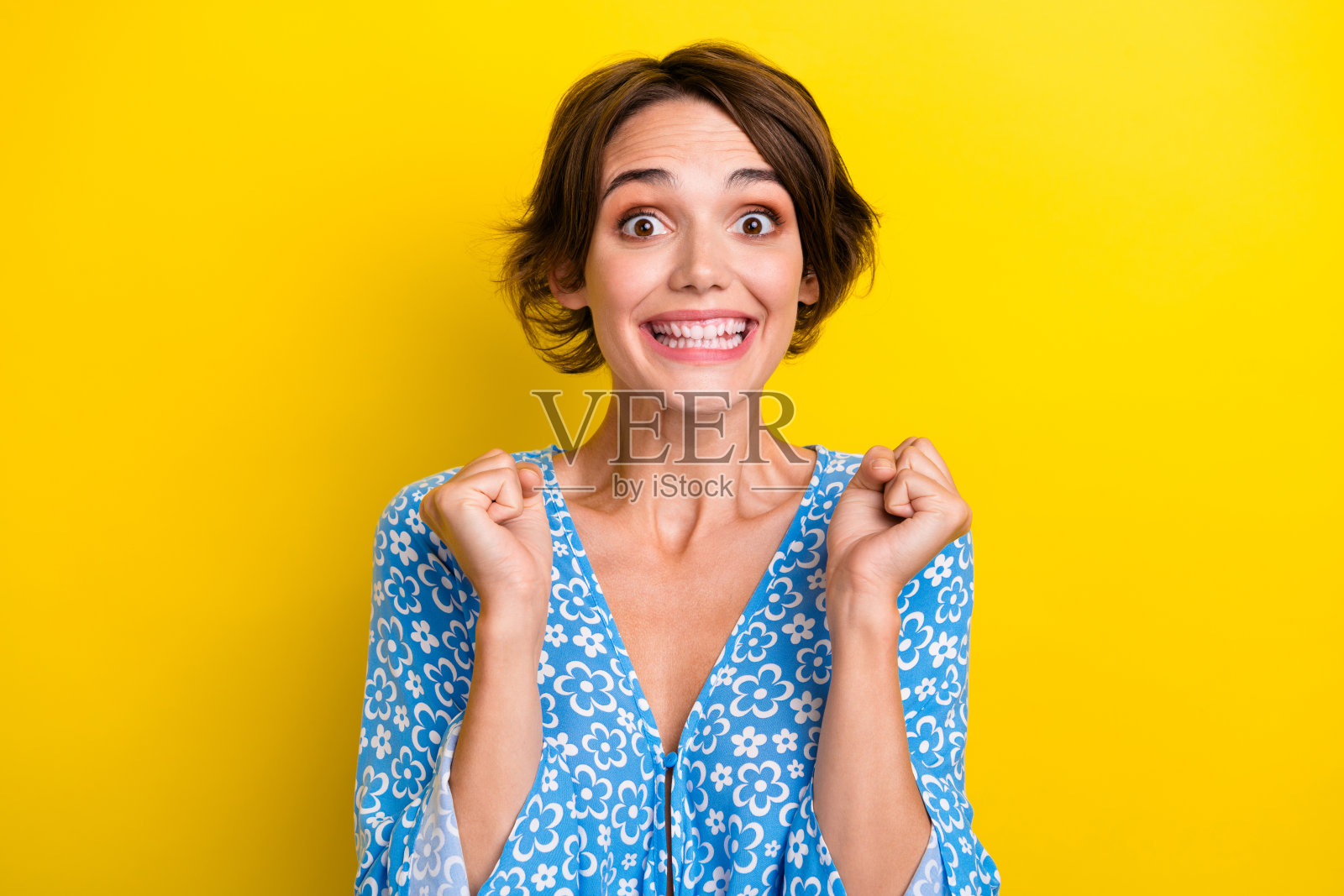 肖像欣喜若狂的女孩与短头发，穿蓝色衬衫，紧握拳头赢得彩票孤立的黄色背景照片摄影图片