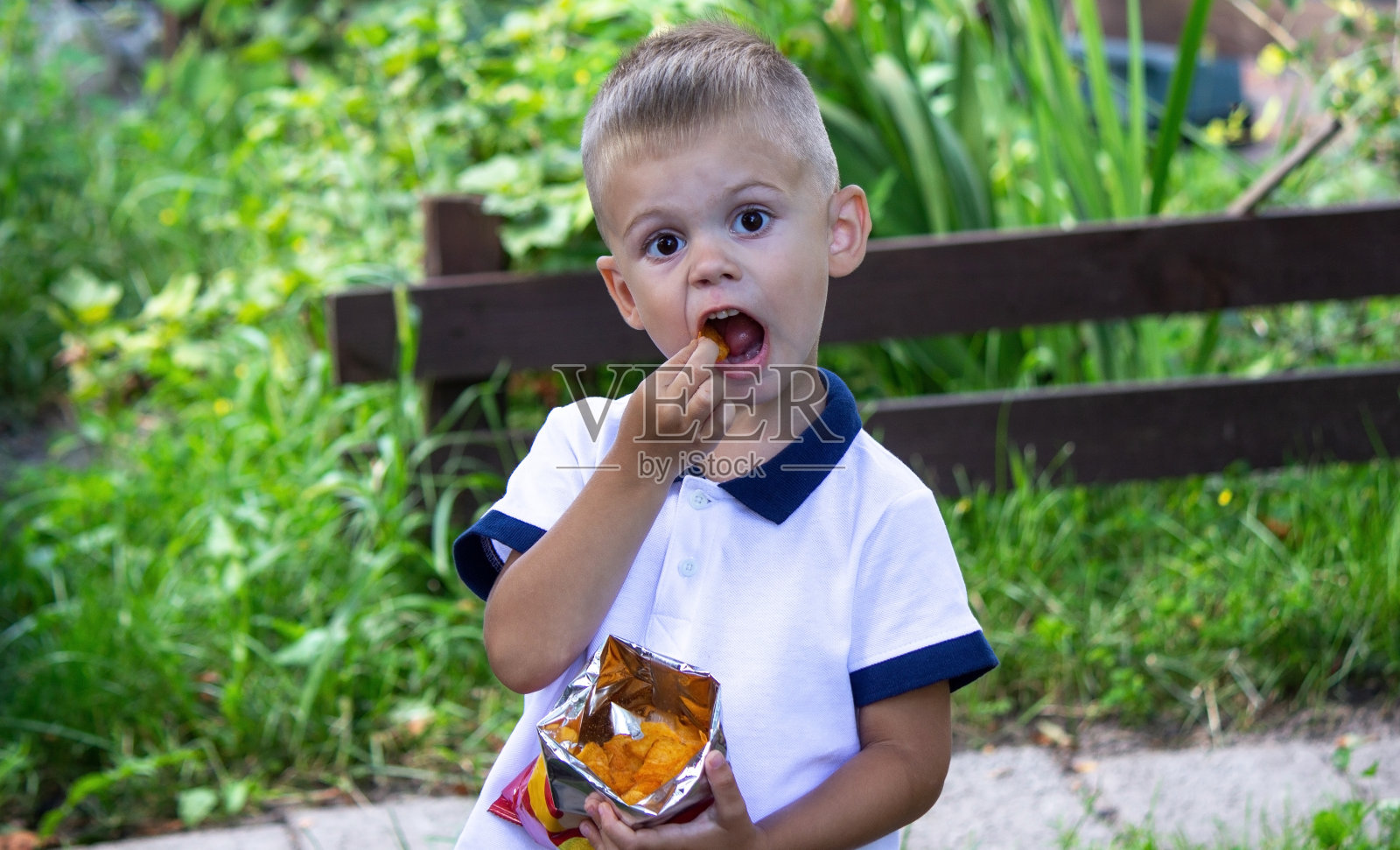 在大自然的背景下，一个孩子正在吃一包薯片。照片摄影图片