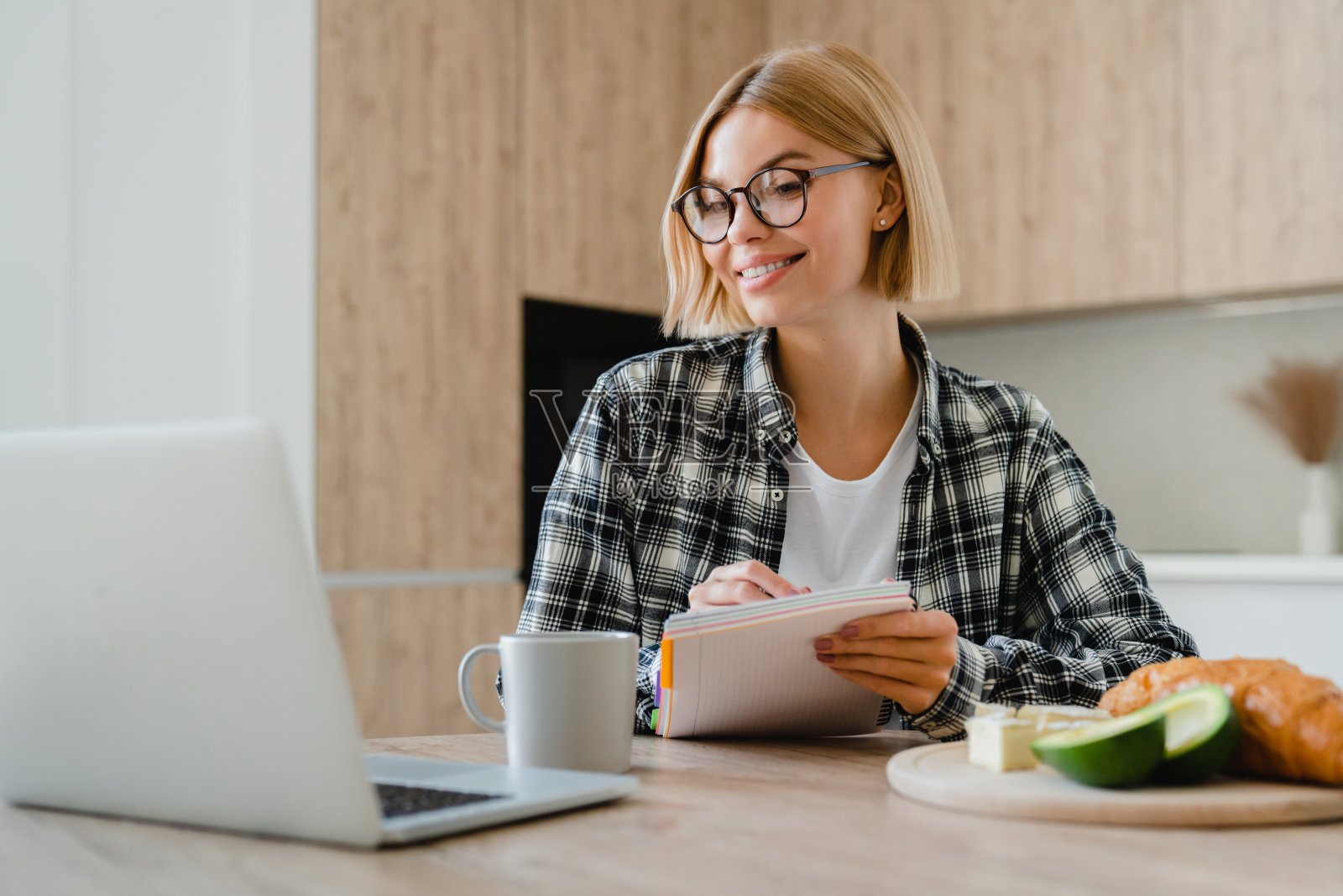 快乐的年轻女子在家里厨房用笔记本电脑做笔记。照片摄影图片