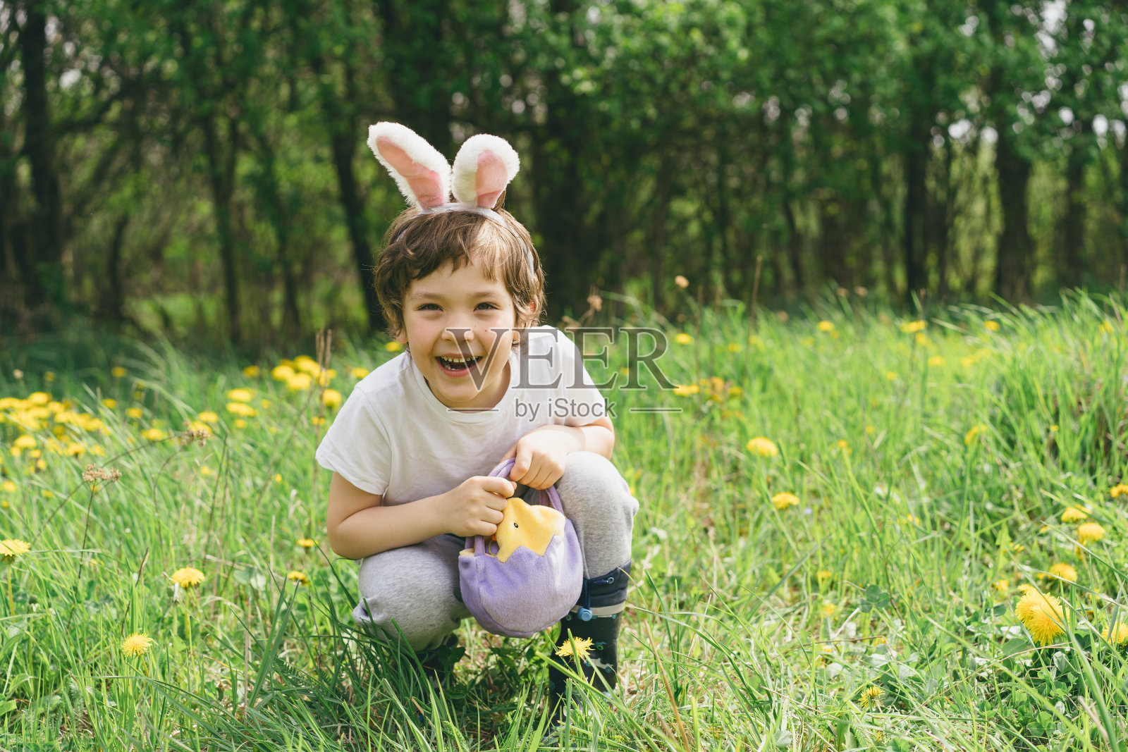 有趣的男孩带着鸡蛋篮子和兔子耳朵在阳光明媚的春天花园里寻找复活节彩蛋照片摄影图片