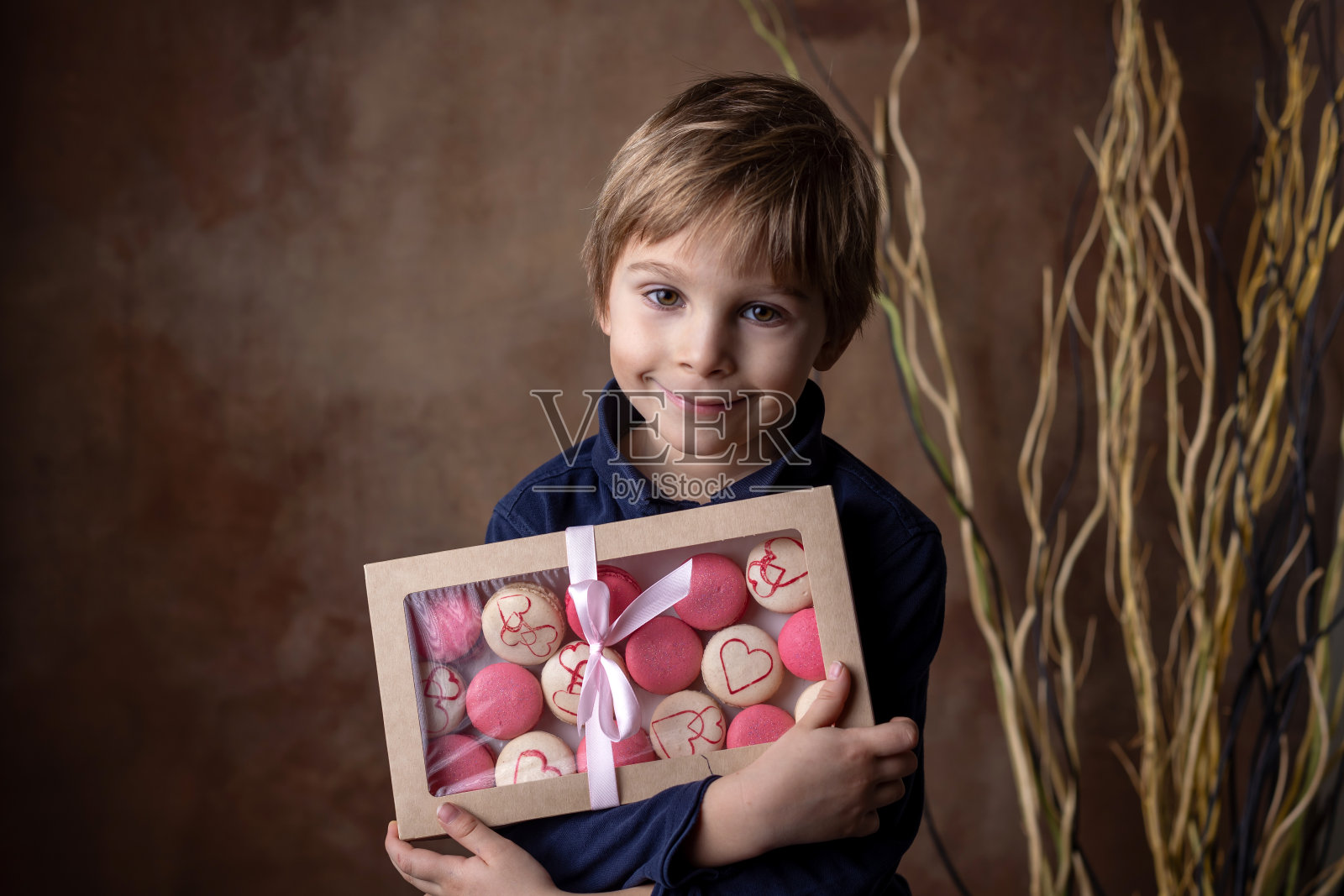 漂亮的金发男孩，拿着装着甜杏仁饼的盒子，作为情人节礼物送给妈妈照片摄影图片