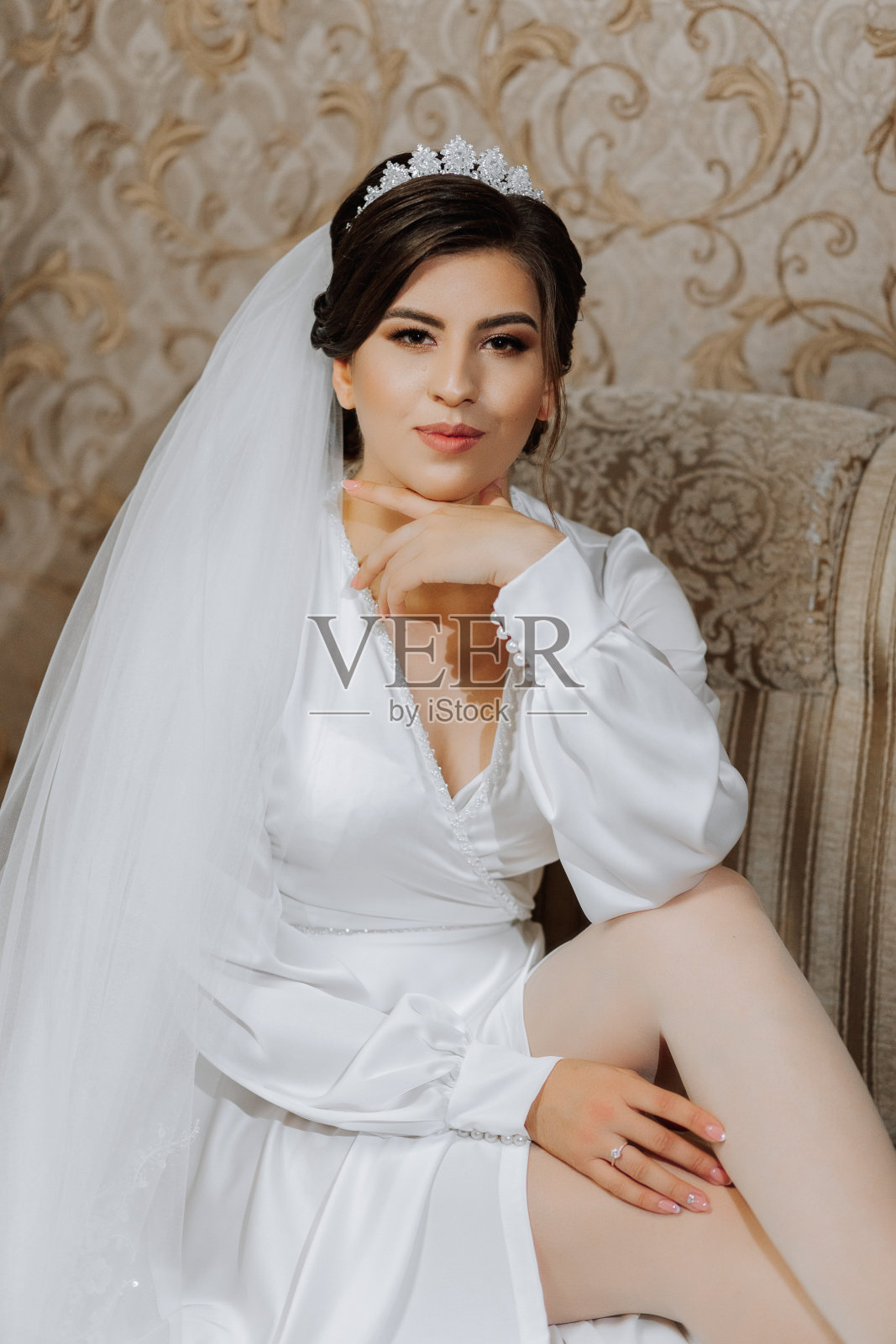 一个美丽的黑发女人的肖像，她穿着迷人的丝绸婚纱，头上戴着皇冠，戴着长长的面纱。为摄影师摆姿势。照片摄影图片