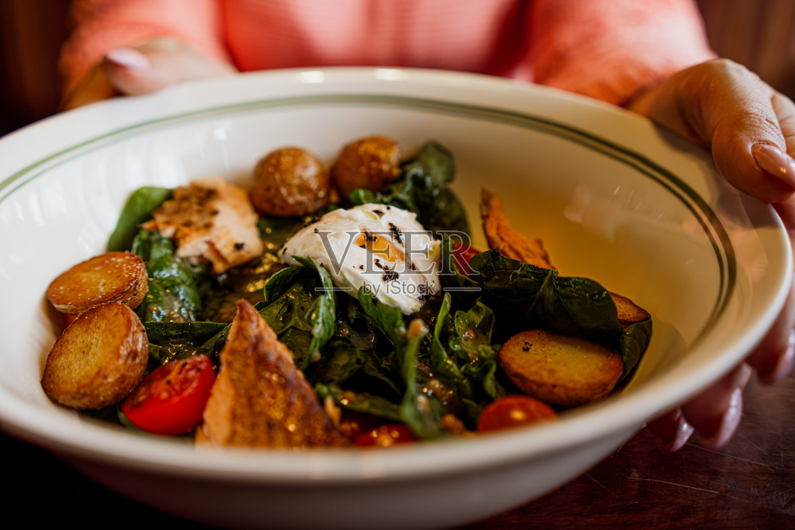一种有烟熏鲑鱼、土豆、圣女果、菠菜和荷包蛋的美味沙拉，装在白色的碗里。照片摄影图片