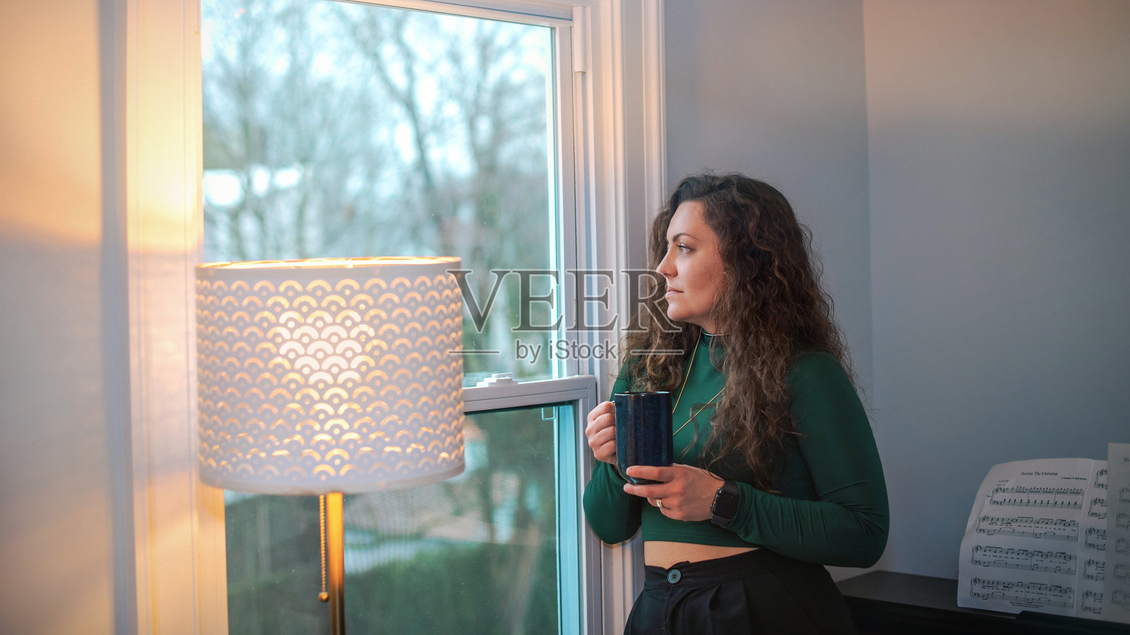 沉思:一头长发的年轻女子端着一杯茶望着窗外。照片摄影图片