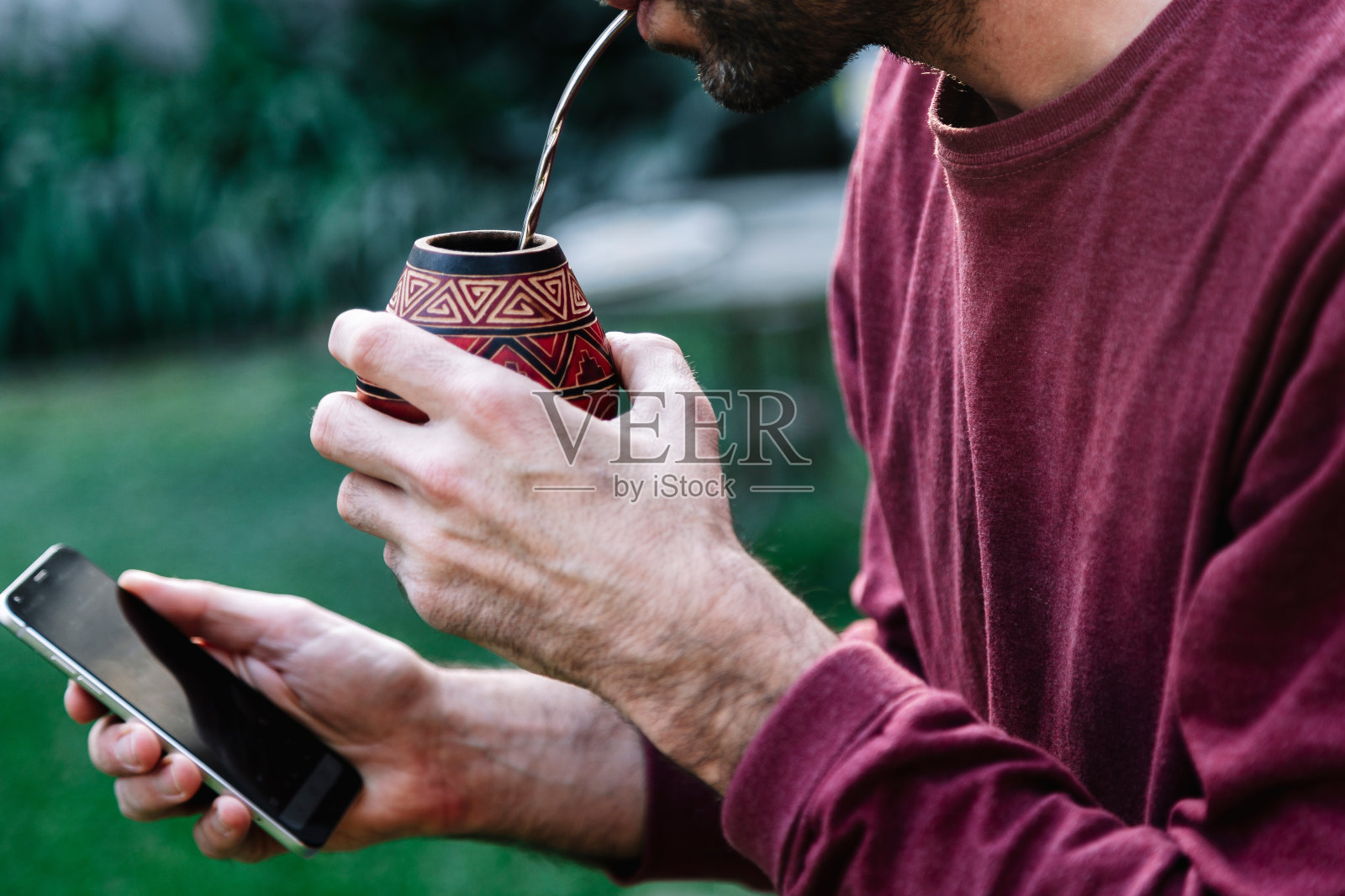 一个男人喝着马黛茶，手里拿着手机。南美的马黛茶。照片摄影图片