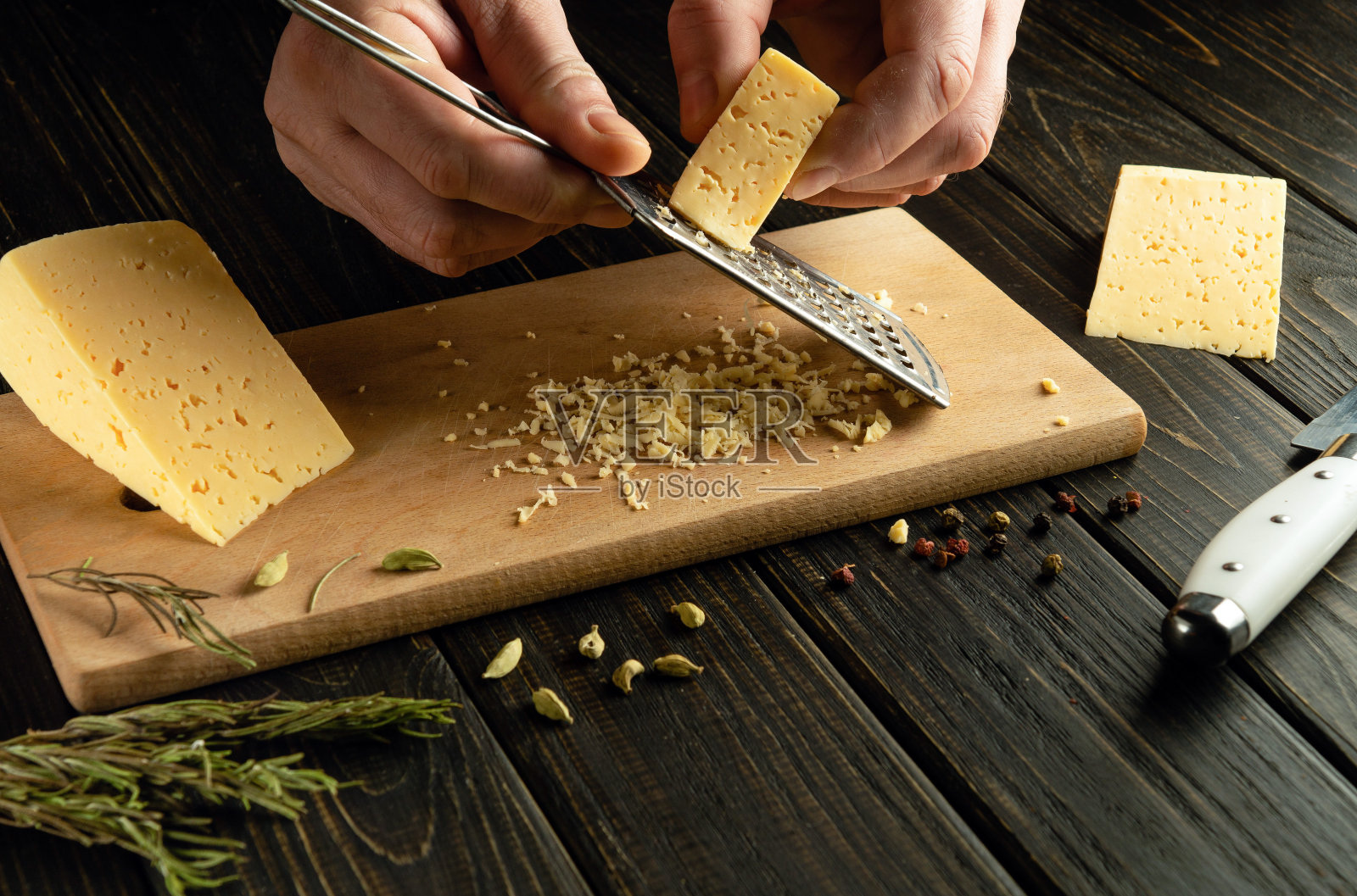 在准备美味的午餐之前，厨师用磨碎器在厨房板上磨碎坚硬的荷兰奶酪。奶酪菜的制作概念照片摄影图片