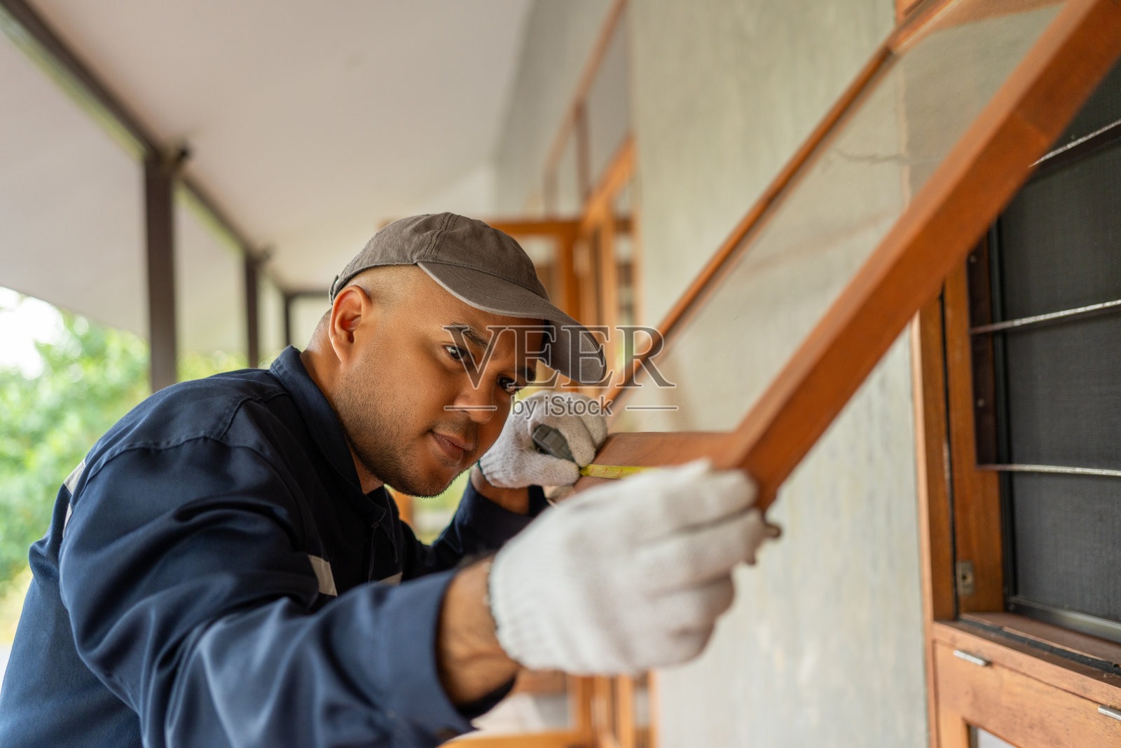 穿着制服的技术工人使用卷尺工具在住宅施工现场测量木窗。维修和解决房屋内的问题照片摄影图片