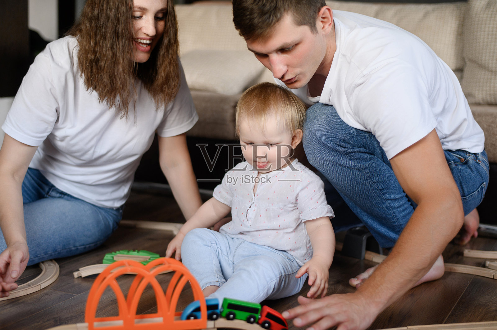 快乐关怀的父母:爸爸妈妈带着孩子玩着木铁路，推着火车，坐在家里的地板上。照片摄影图片