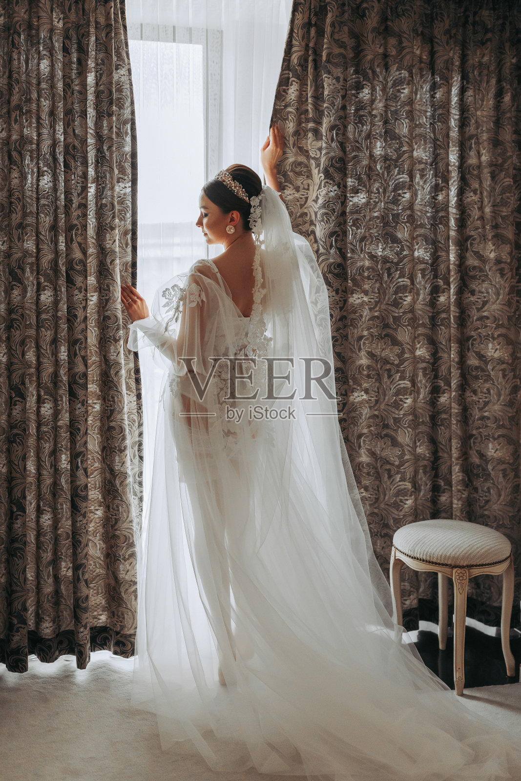 一位穿着透明长袍、头戴王冠、留着婚礼发型的美丽少女，正在皇家室内酒店准备婚礼。长面纱，自然光，人像照片照片摄影图片