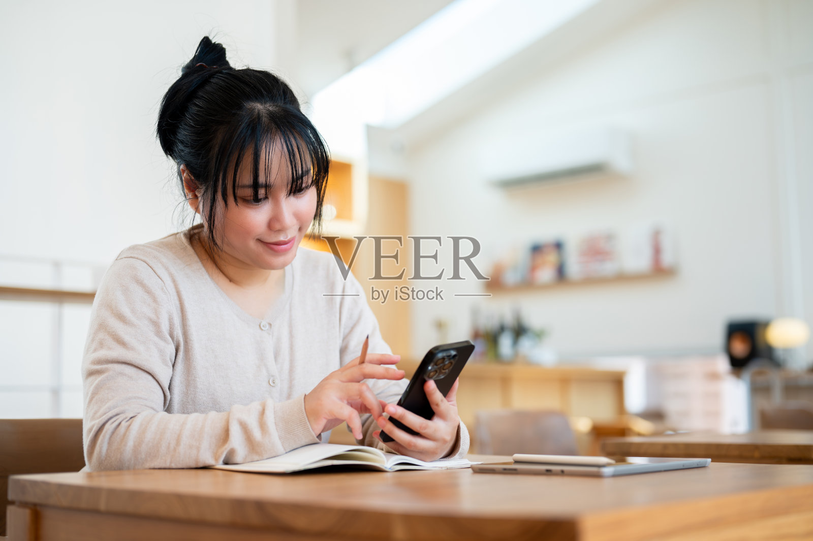 一位快乐的亚洲女性坐在舒适的咖啡店里玩着她的智能手机。照片摄影图片