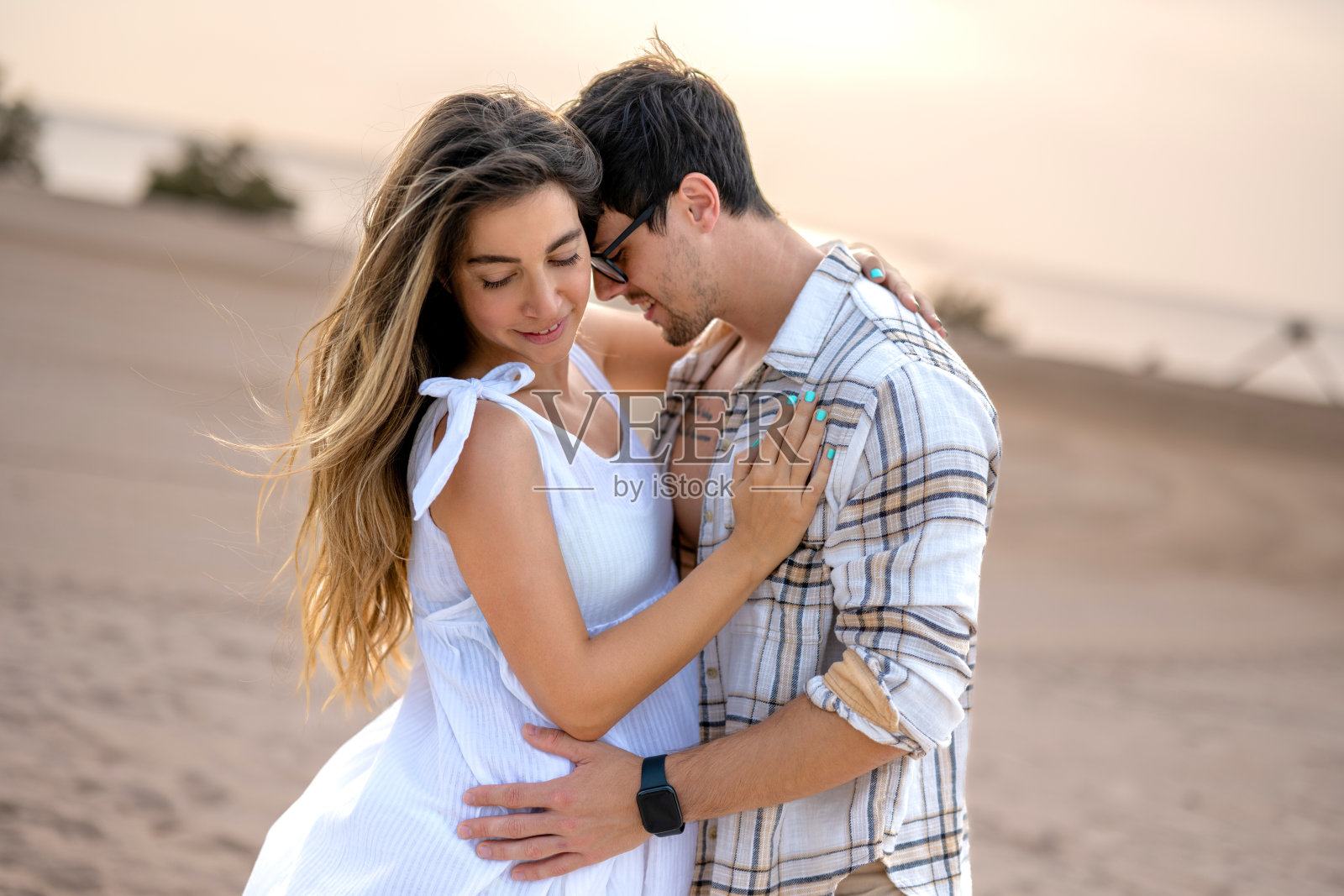 快乐的男人在沙滩上拥抱孕妇，享受美好时光照片摄影图片