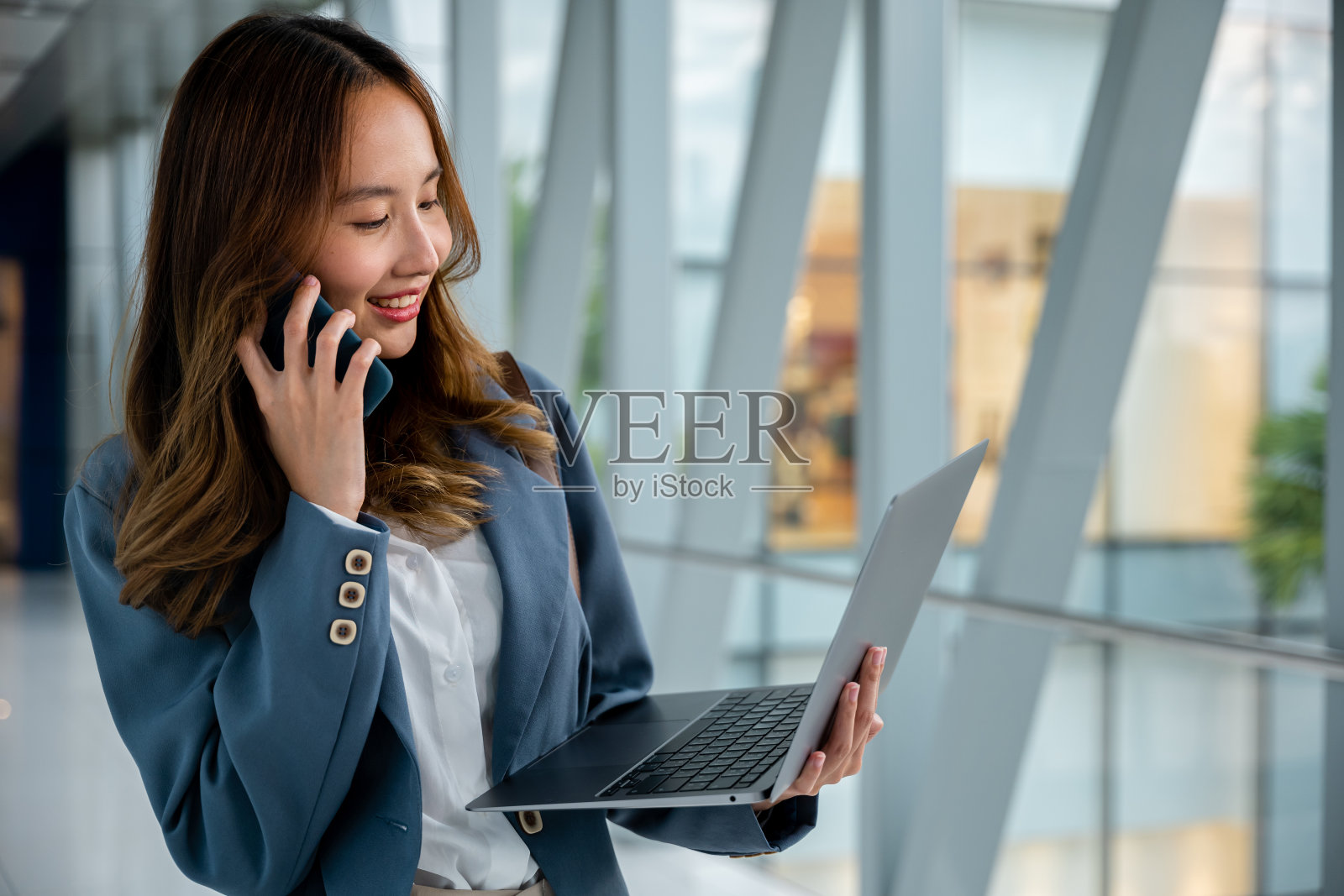 年轻女子在机场用笔记本电脑和手机同时处理多项任务照片摄影图片