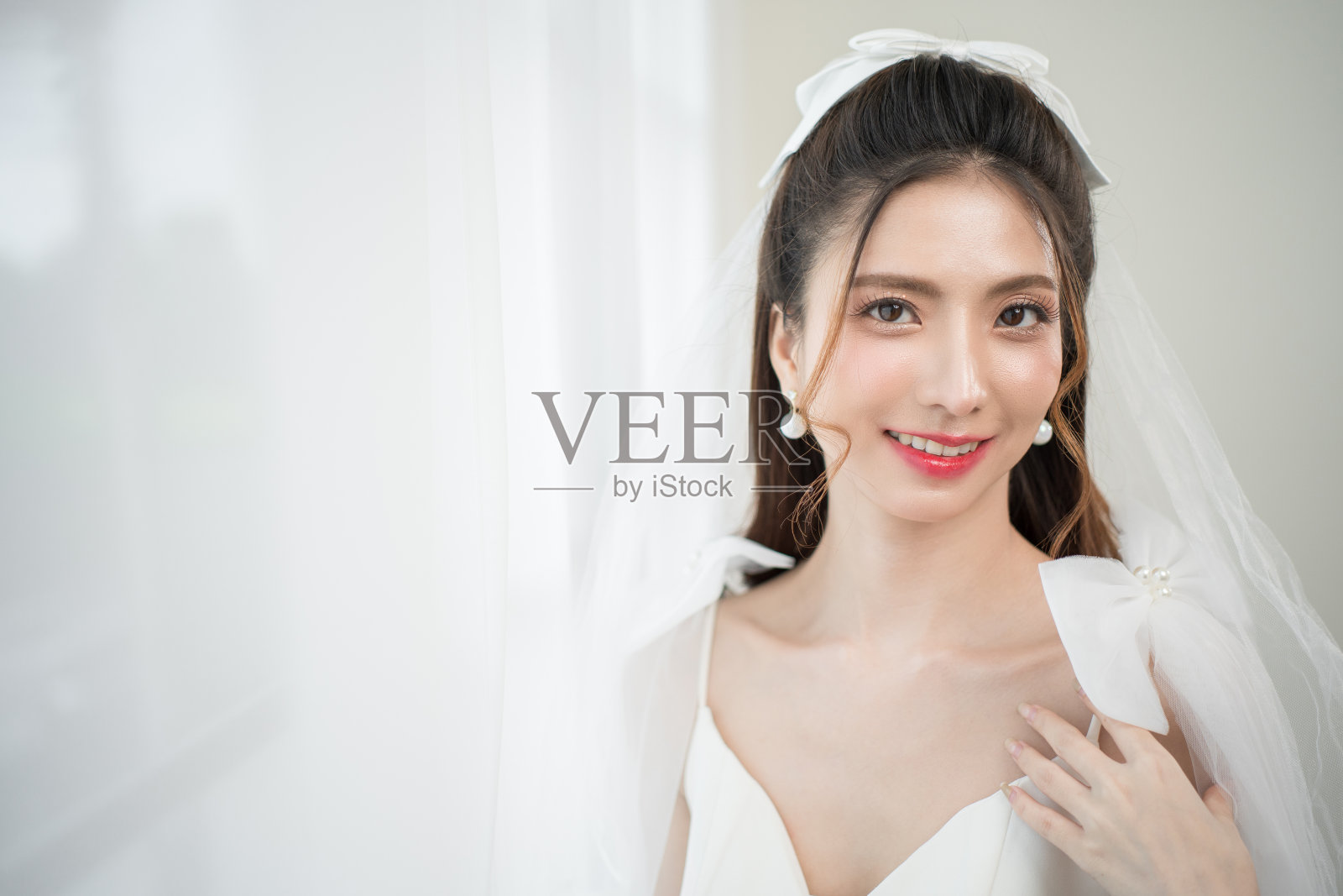 美丽的亚洲新娘与时尚的婚礼发型和化妆。年轻美丽的新娘的肖像在白色的房间里拍摄的婚礼工作室。照片摄影图片