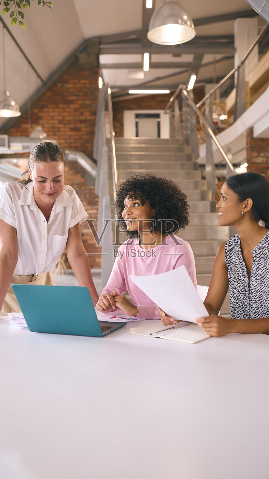 三个年轻的女商人在现代办公室开会，围坐在桌子旁一起用笔记本电脑工作照片摄影图片
