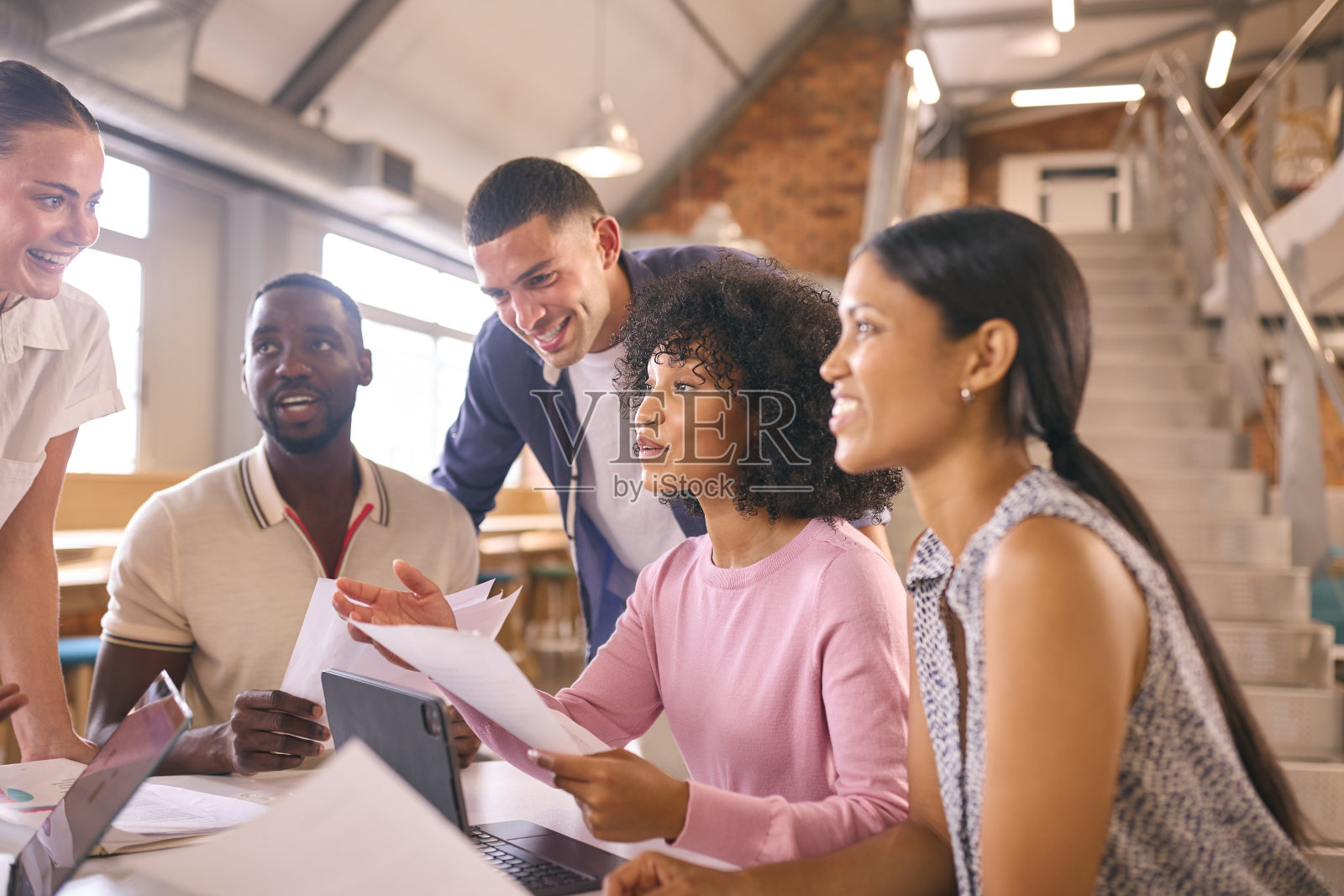 现代开放式办公中，跨文化商务团队围坐办公桌讨论文件照片摄影图片