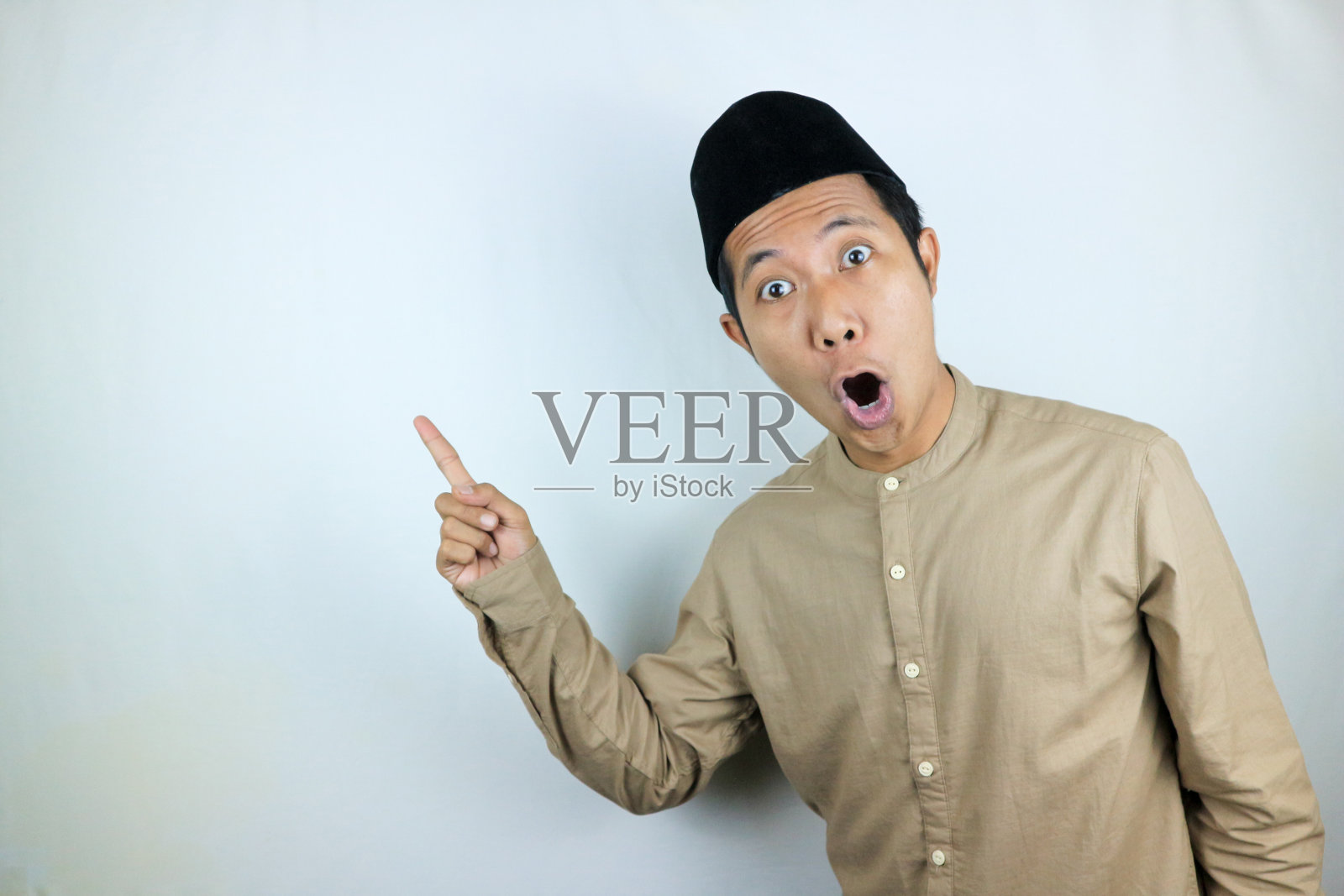 滑稽的面部表情震惊和惊讶的亚洲穆斯林男子戴着帽子指着一边照片摄影图片