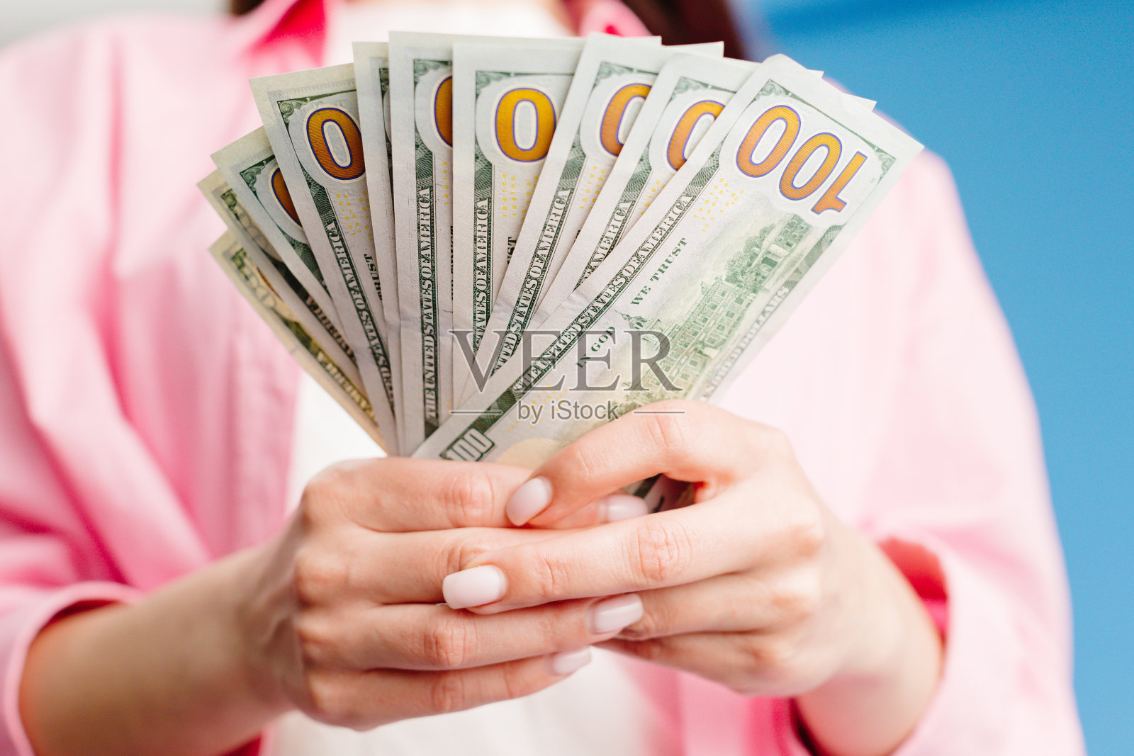 女性手数一叠百元大钞的特写，蓝色背景照片摄影图片