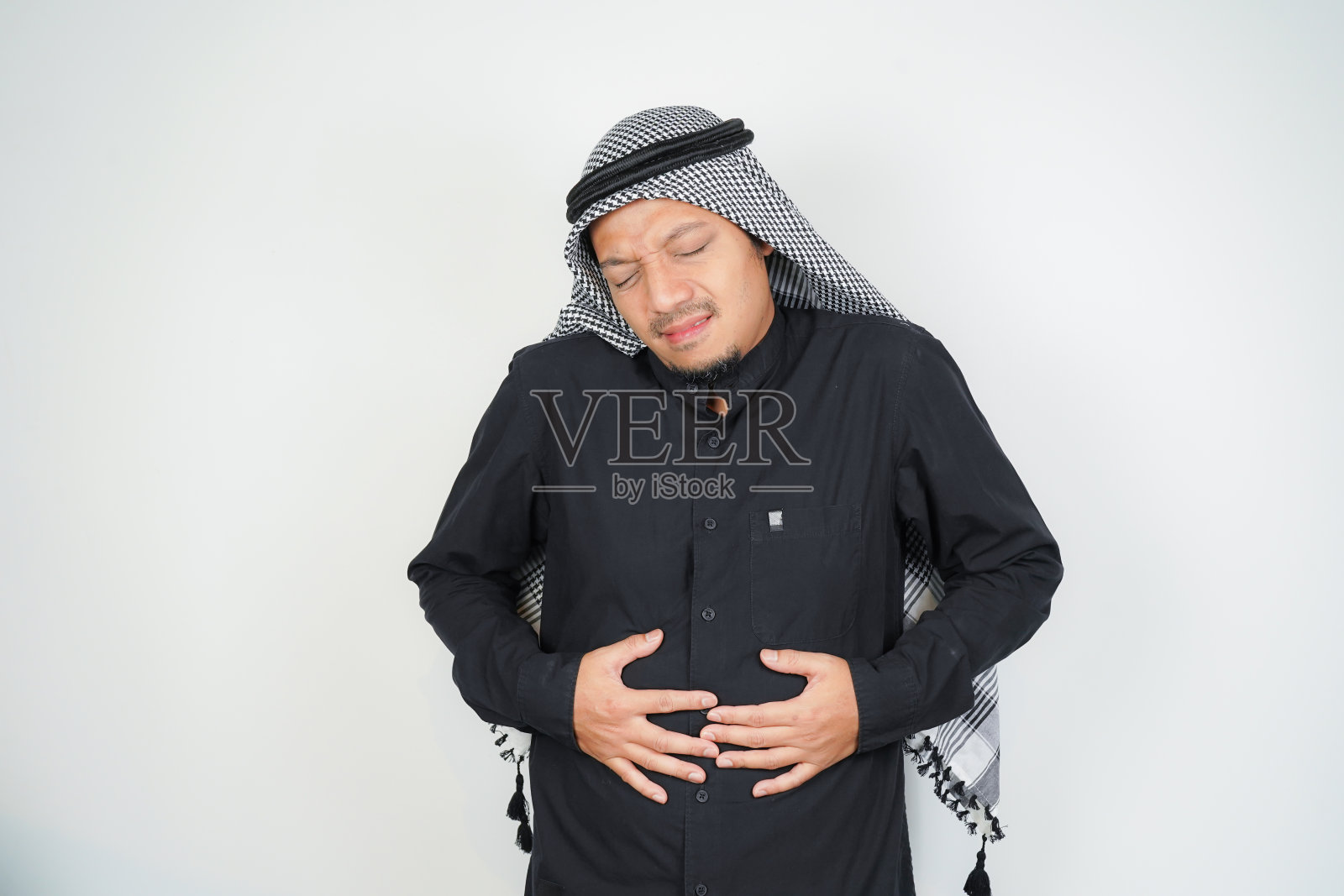 穆斯林男子戴着阿拉伯头巾索邦有胃痛，弯腰，双手捂胃，胃痉挛，胃痛照片摄影图片