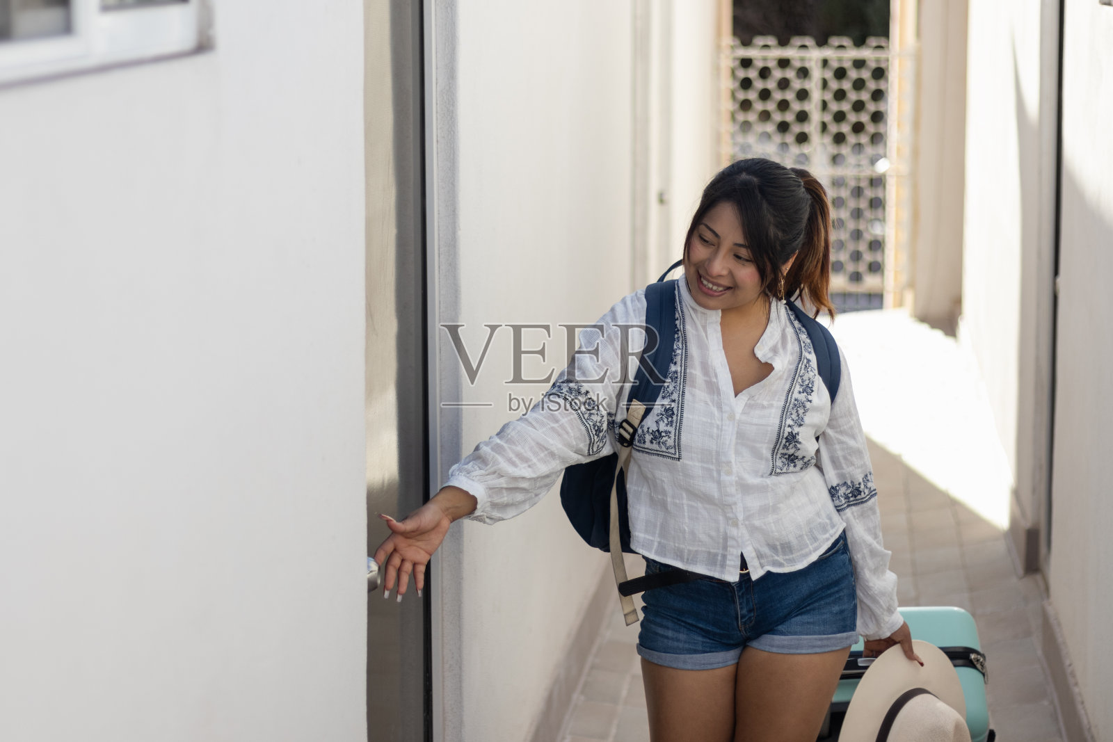 20多岁的美女带着微笑独自旅行;打开她在旅行中租的公寓的门，她正在拉着她的手提箱，里面有复印空间照片摄影图片