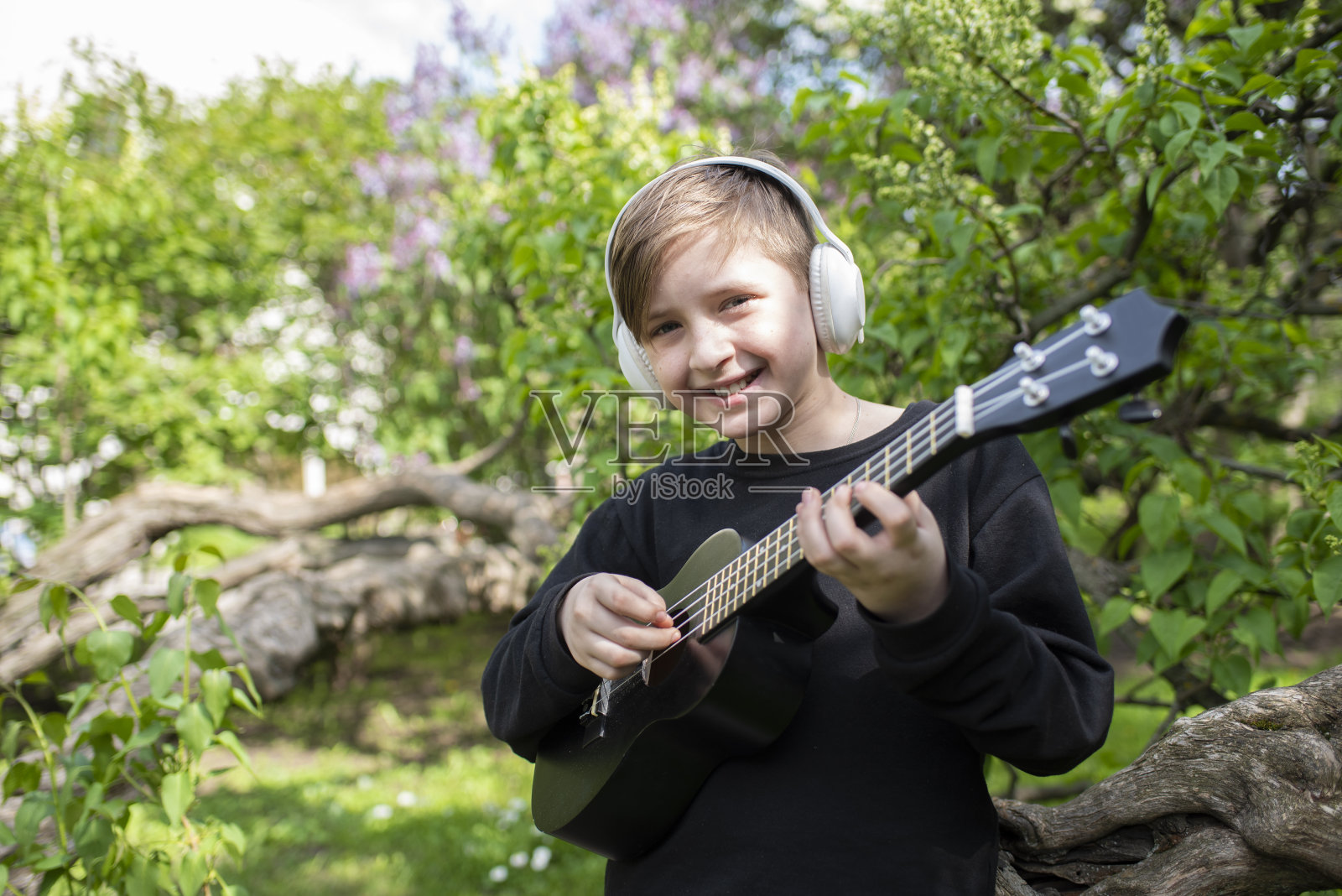 小男孩在城市公园里弹尤克里里。照片摄影图片