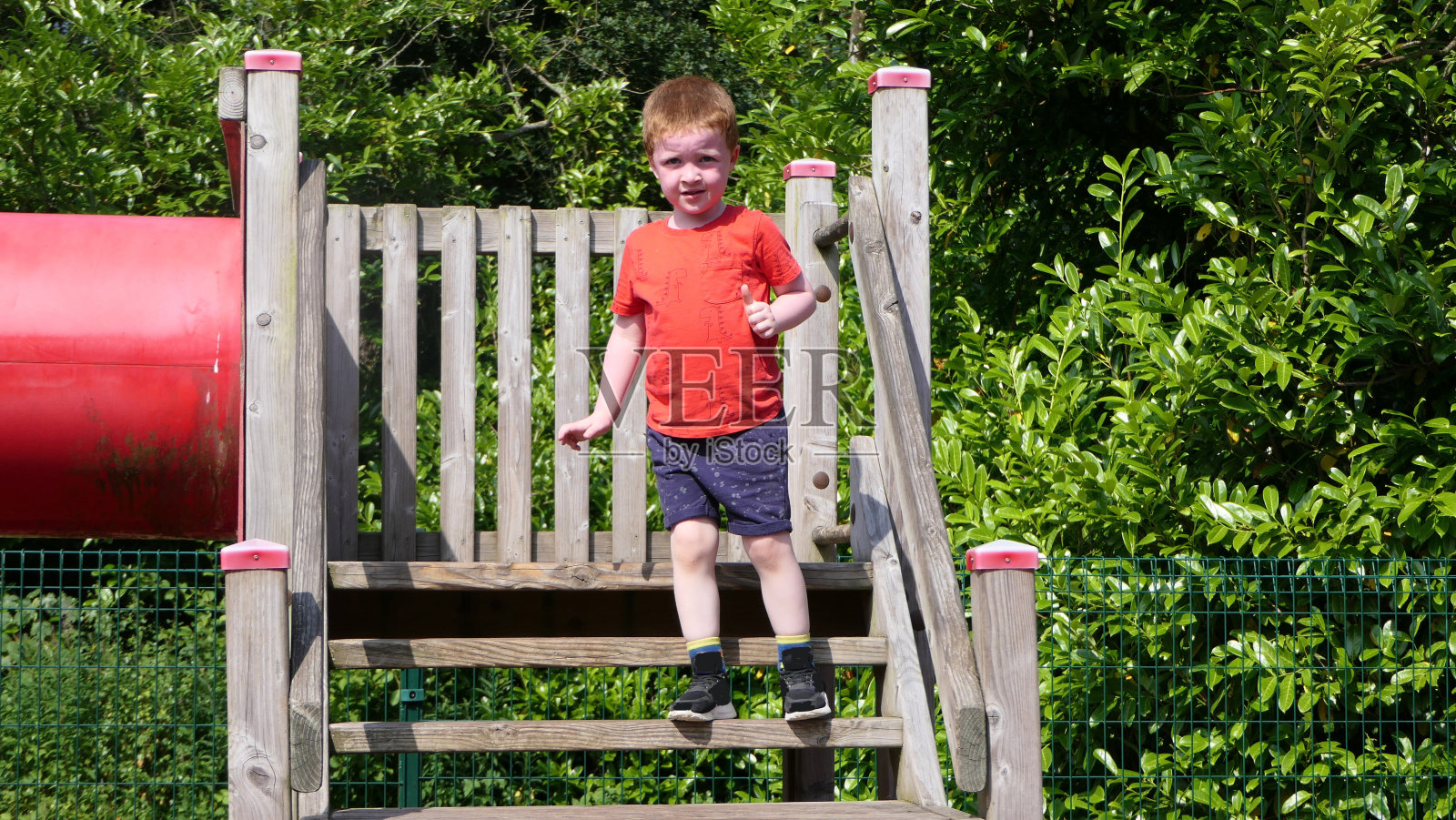 在一个阳光明媚的日子里，穿着红色t恤的红发男孩在游乐场玩得很开心照片摄影图片