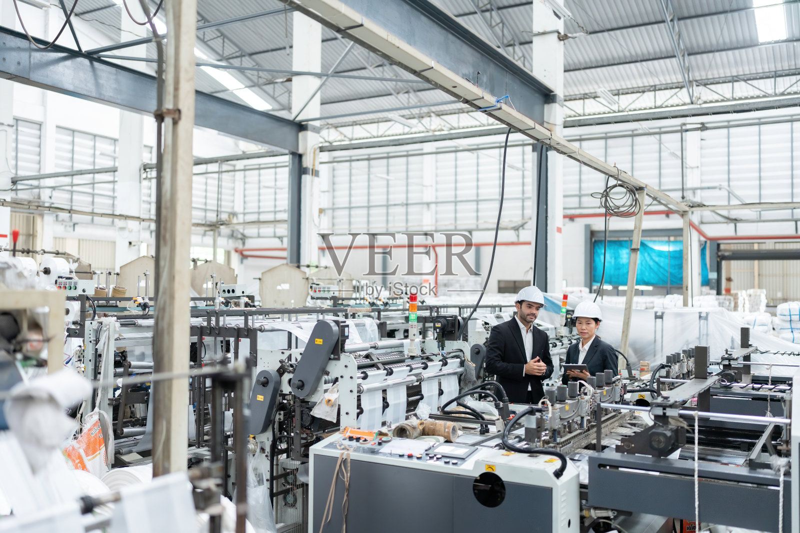 广角镜头，一位美国男工程师主持人和一位全球大型企业的女建筑师在一个仓库里被机器包围的汽车工业工厂里一起工作。照片摄影图片