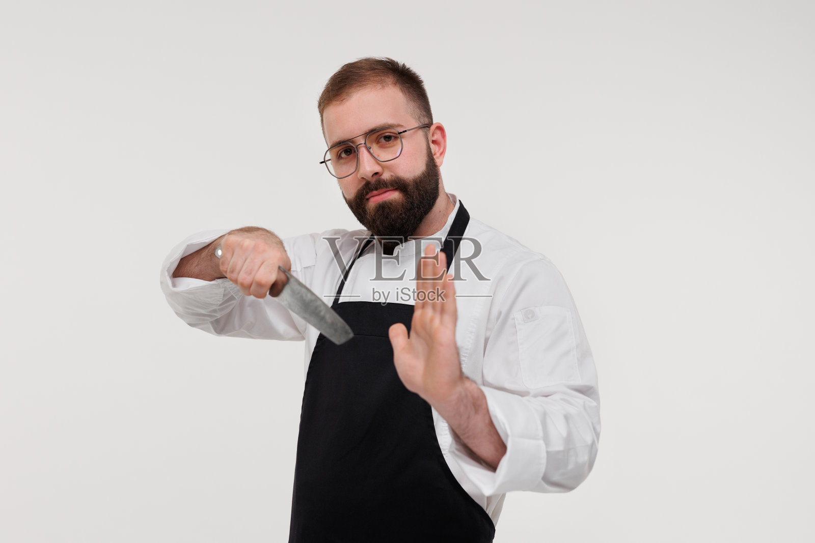 工作室拍摄的一个快乐的留胡子的年轻厨师手里拿着锋利的刀在白色的背景。照片摄影图片