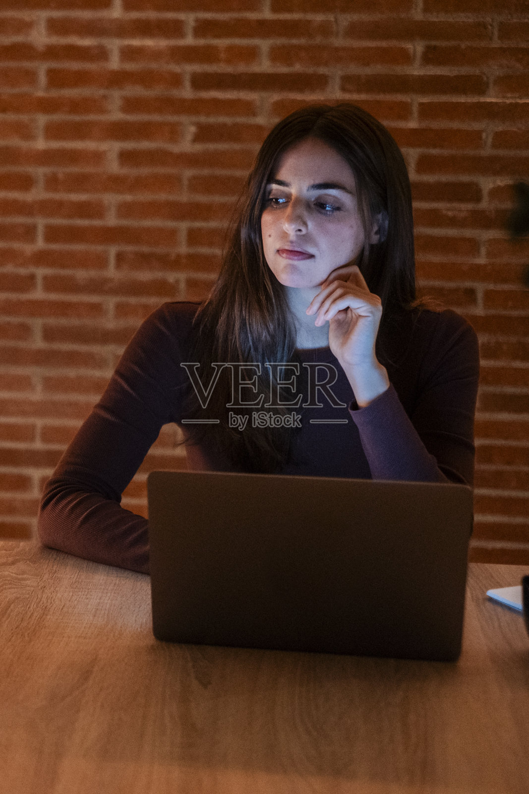 年轻漂亮的微笑女人晚上在家里用笔记本电脑。悲伤的女孩看着电脑。快乐的人们坐在客厅的书桌前。有进取心，远程办公，工作勤奋的人。照片摄影图片