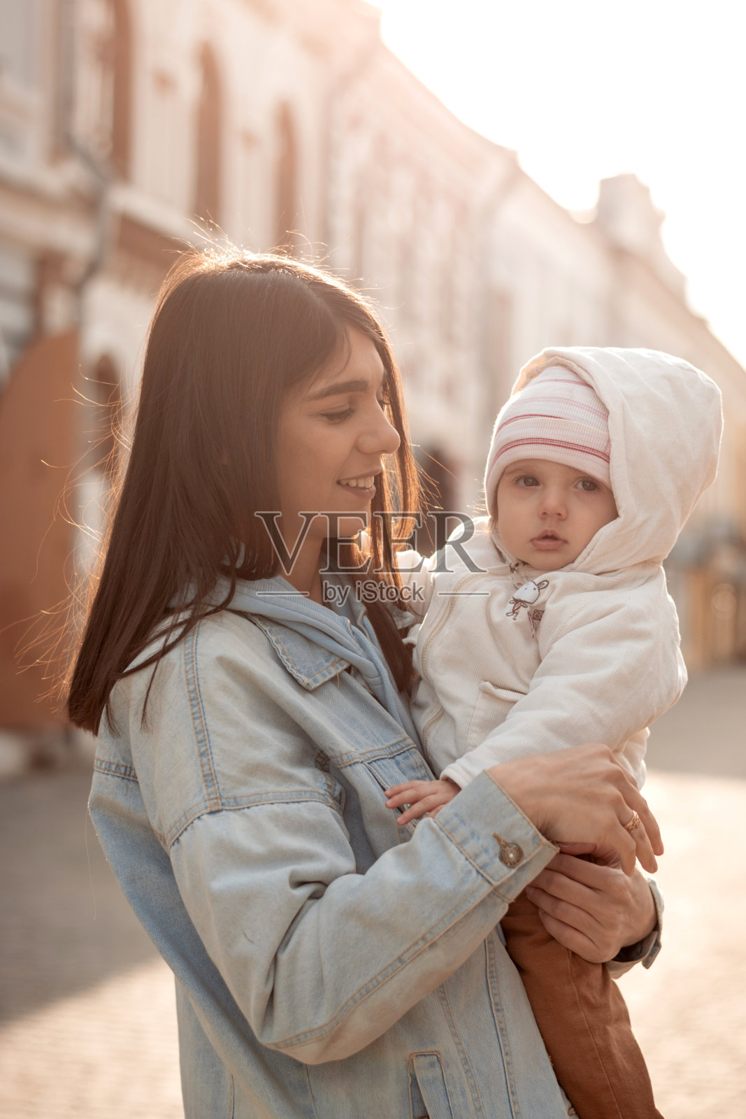 一位年轻快乐的黑发妇女带着她的小女儿走在城市的街道上。家庭的概念。快乐的母亲。照片摄影图片