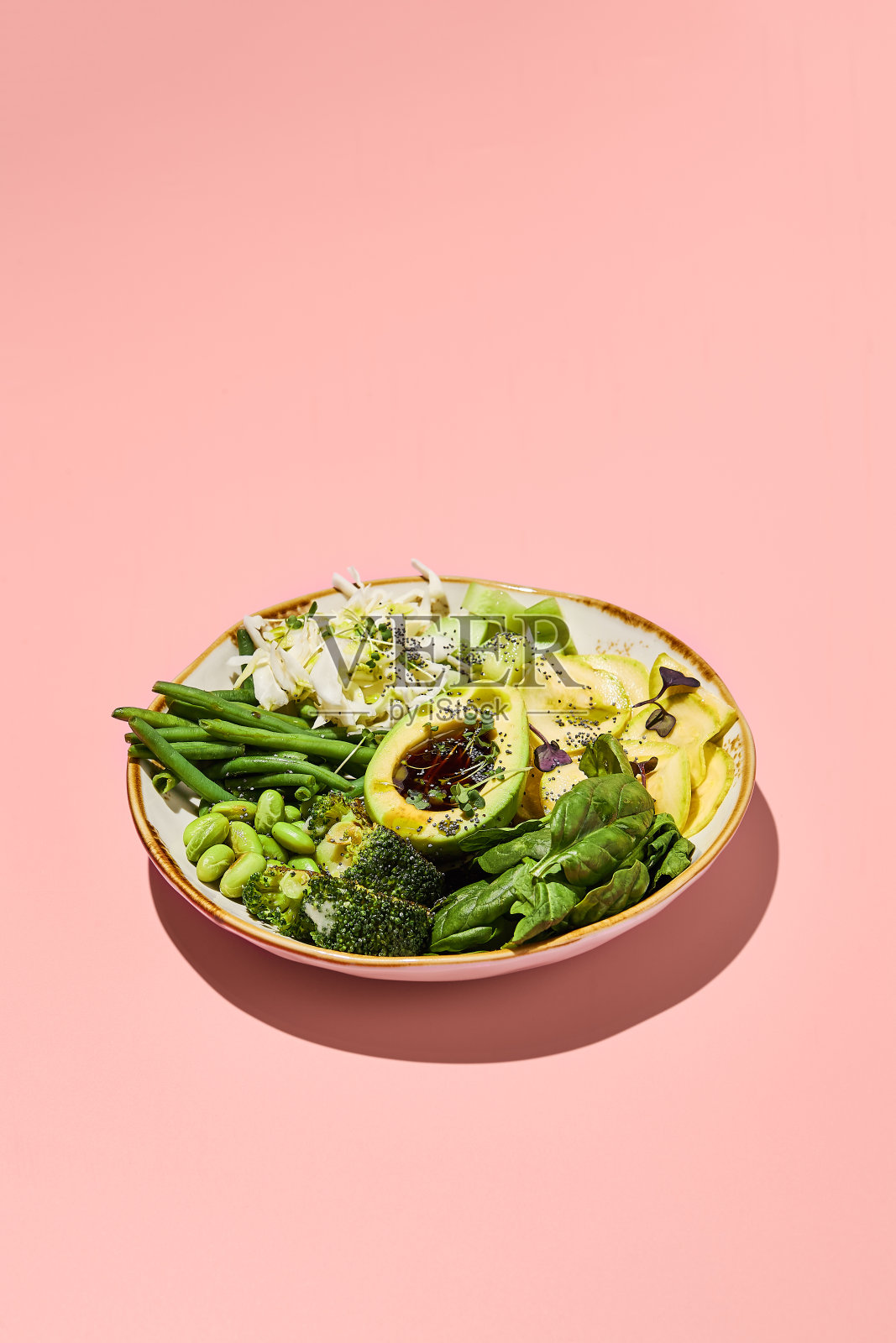 绿色沙拉碗，有鳄梨、毛豆、卷心菜、西葫芦、西兰花和青豆，粉红色的背景。完美的清洁饮食生活方式照片摄影图片