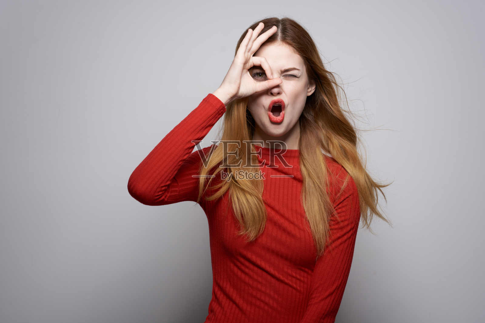 穿着红裙子的快乐女人摆出奢华的手势工作室照片摄影图片