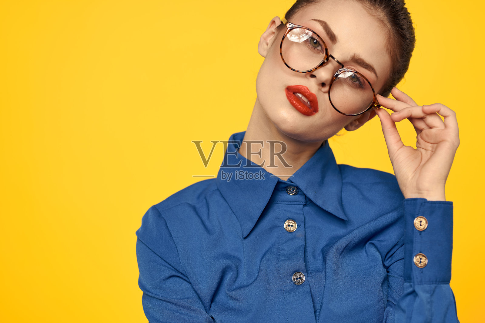 一位身穿蓝色衬衫、戴着眼镜、脸上涂着亮色妆容的女士正在用手做手势照片摄影图片