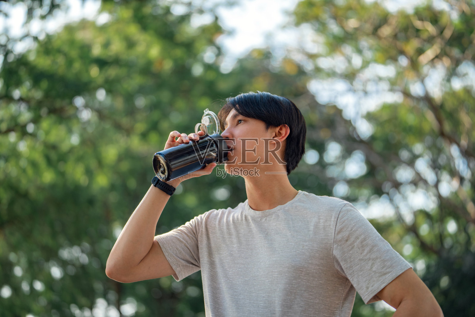 健身，穿着运动服的亚洲男子在公园慢跑时从瓶子里喝水。健康运动男性从休息或休息后马拉松或短跑，健康。照片摄影图片