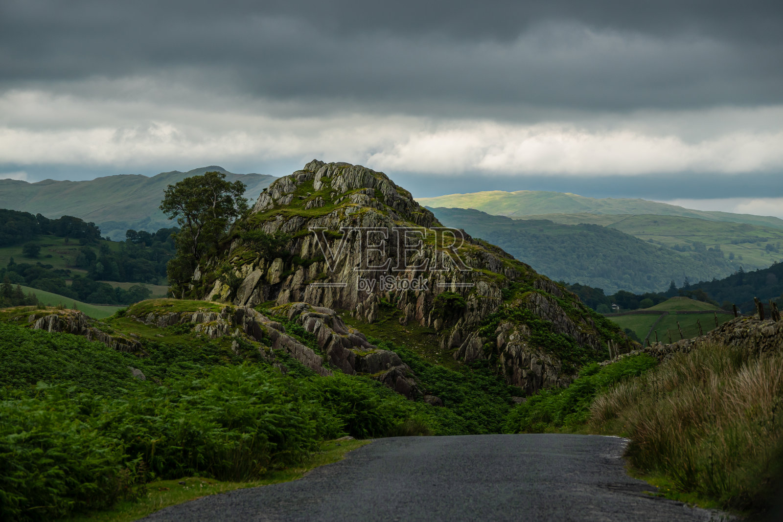 道路将视线引向湖区丘陵景观中的岩石峰顶照片摄影图片