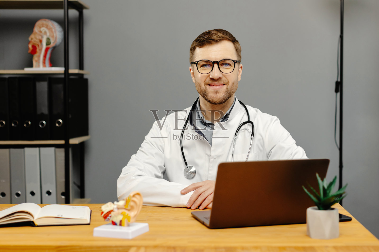 医生拿着笔记本电脑坐在办公桌前照片摄影图片