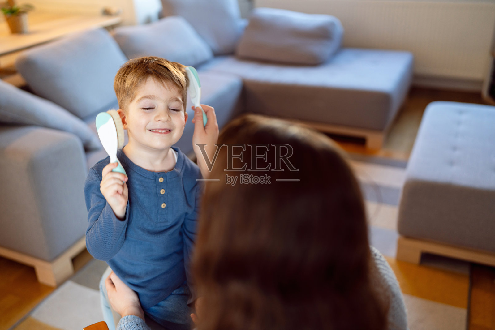 蹒跚学步的小男孩在妈妈给他梳头的时候玩梳子照片摄影图片