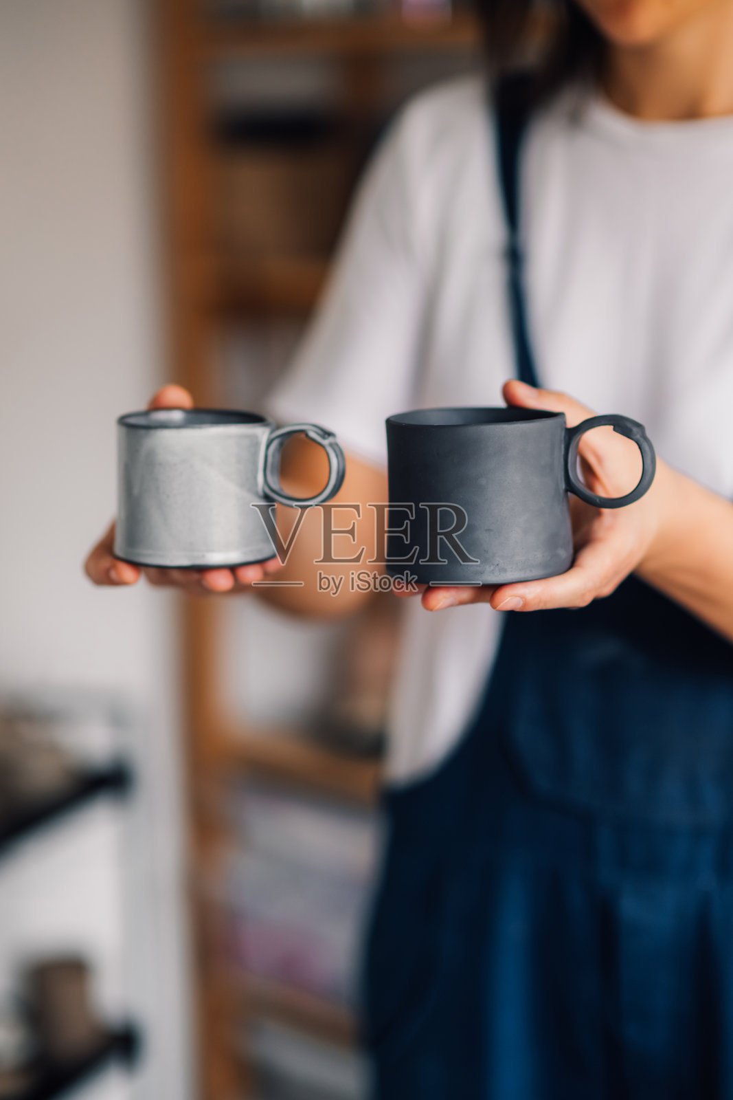 陶艺设计师在陶艺工作室拿着陶土马克杯的特写。照片摄影图片